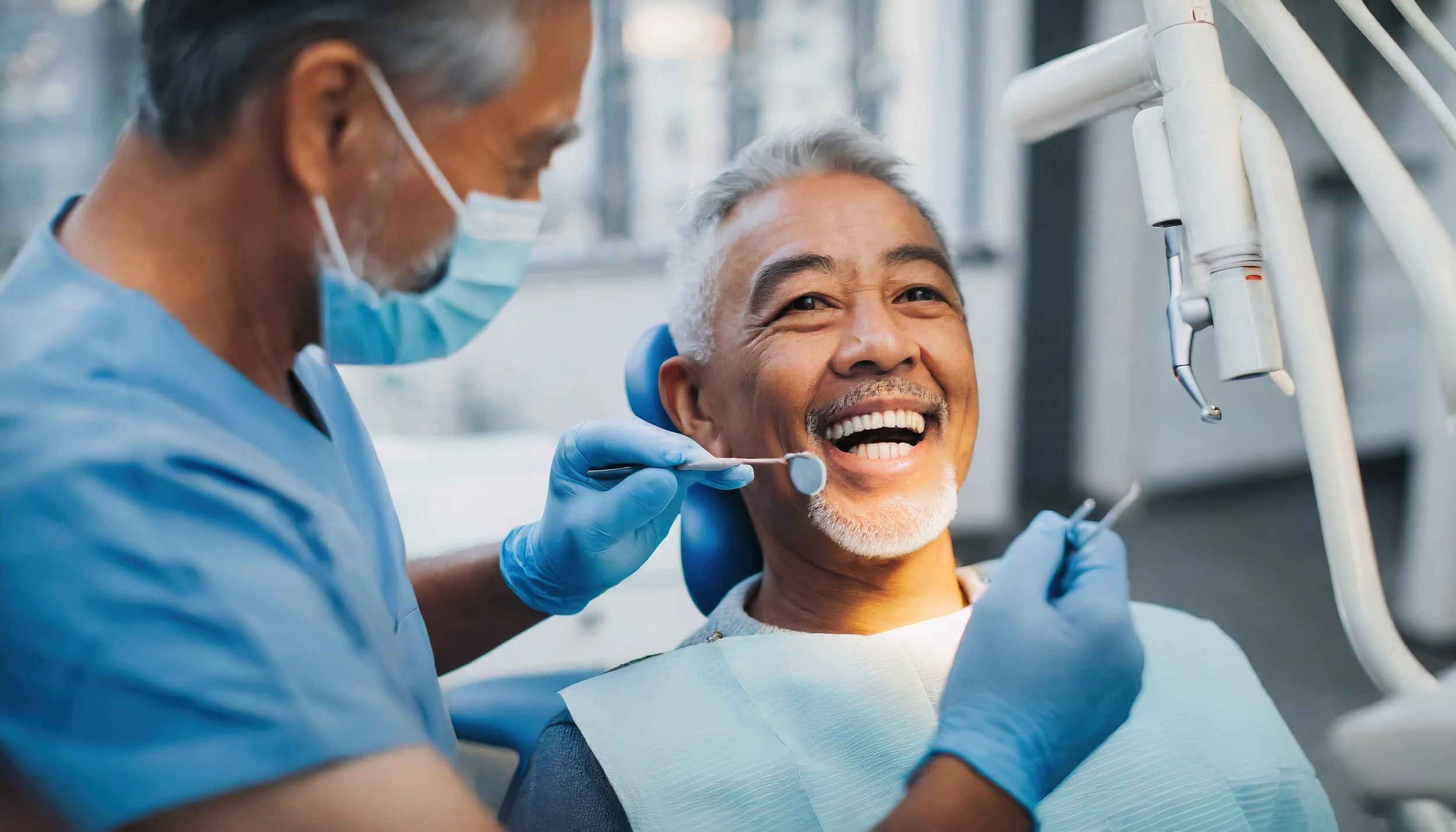 A dentist wearing a mask and gloves is examining and cleaning the teeth of an elderly male patient who is seated in a dental chair, smiling.