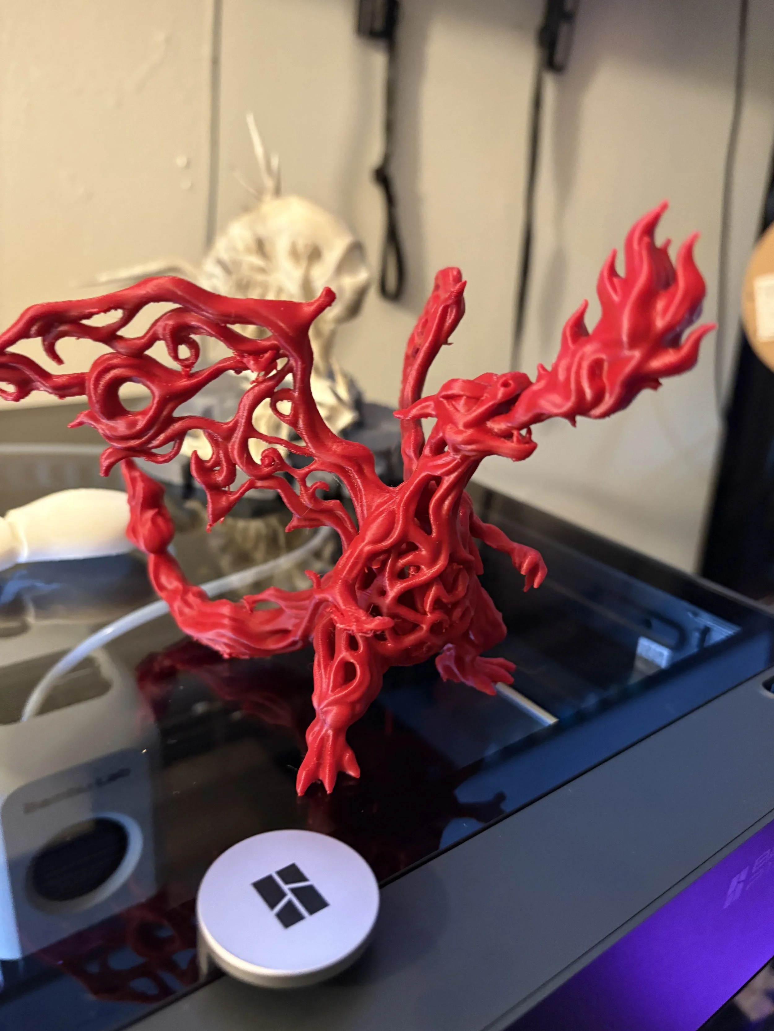 A red, abstract, tree-like sculpture on top of a black surface with a Microsoft sticker visible in the foreground. In the background, a beige wall with an outline of a skull.