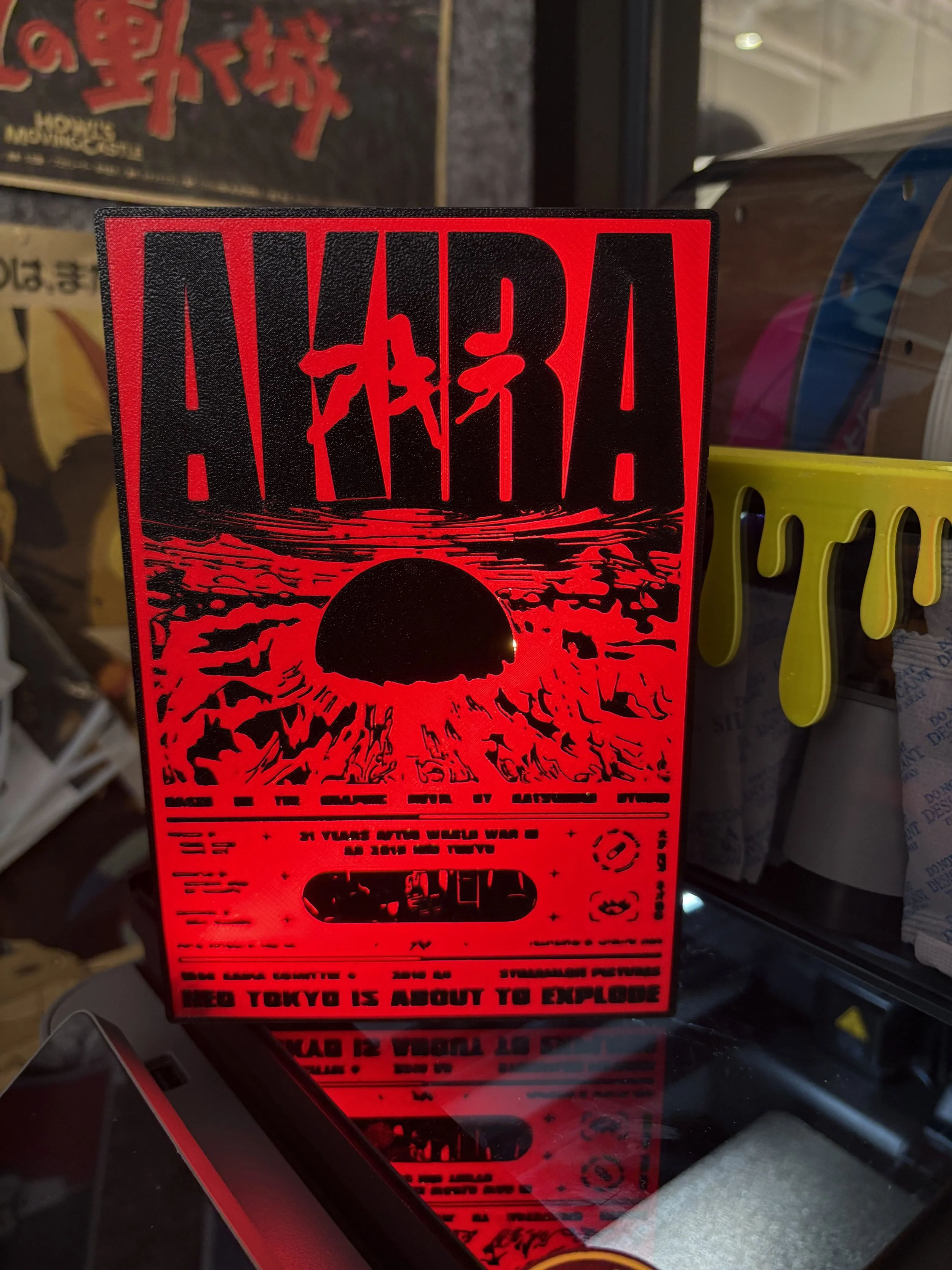A bright red warning sign with the text "WARNING!" at the top, and a black silhouette of a nuclear explosion with a mushroom cloud. The sign includes the phrase "NEED TOKYO IS ABOUT TO EXPLODE" at the bottom, warning of imminent danger.