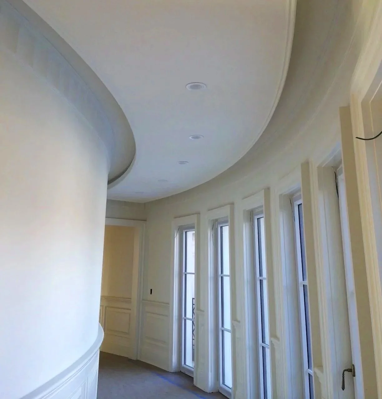 Interior of a room with large windows, a curved ceiling with recessed lighting, and cream-colored walls with decorative trim.
