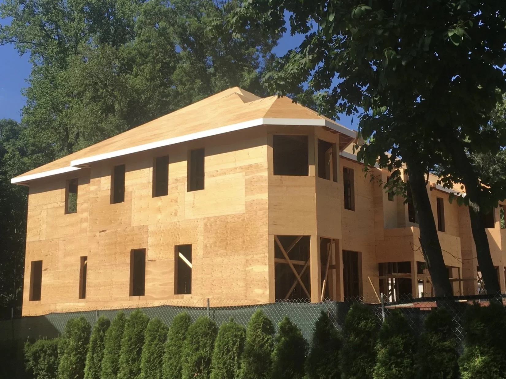 Unfinished wooden house under construction surrounded by trees, with a blue sky overhead.