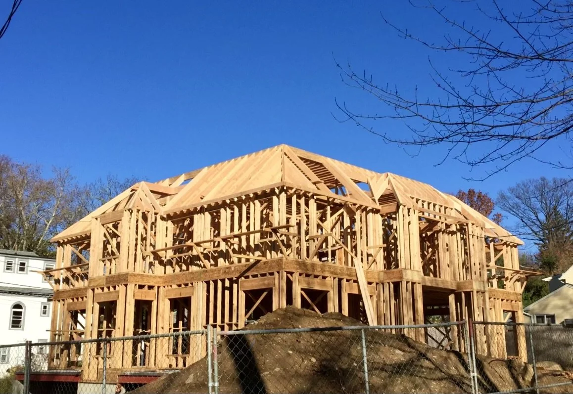 Wooden framing of a house under construction with blue sky background and bare trees.