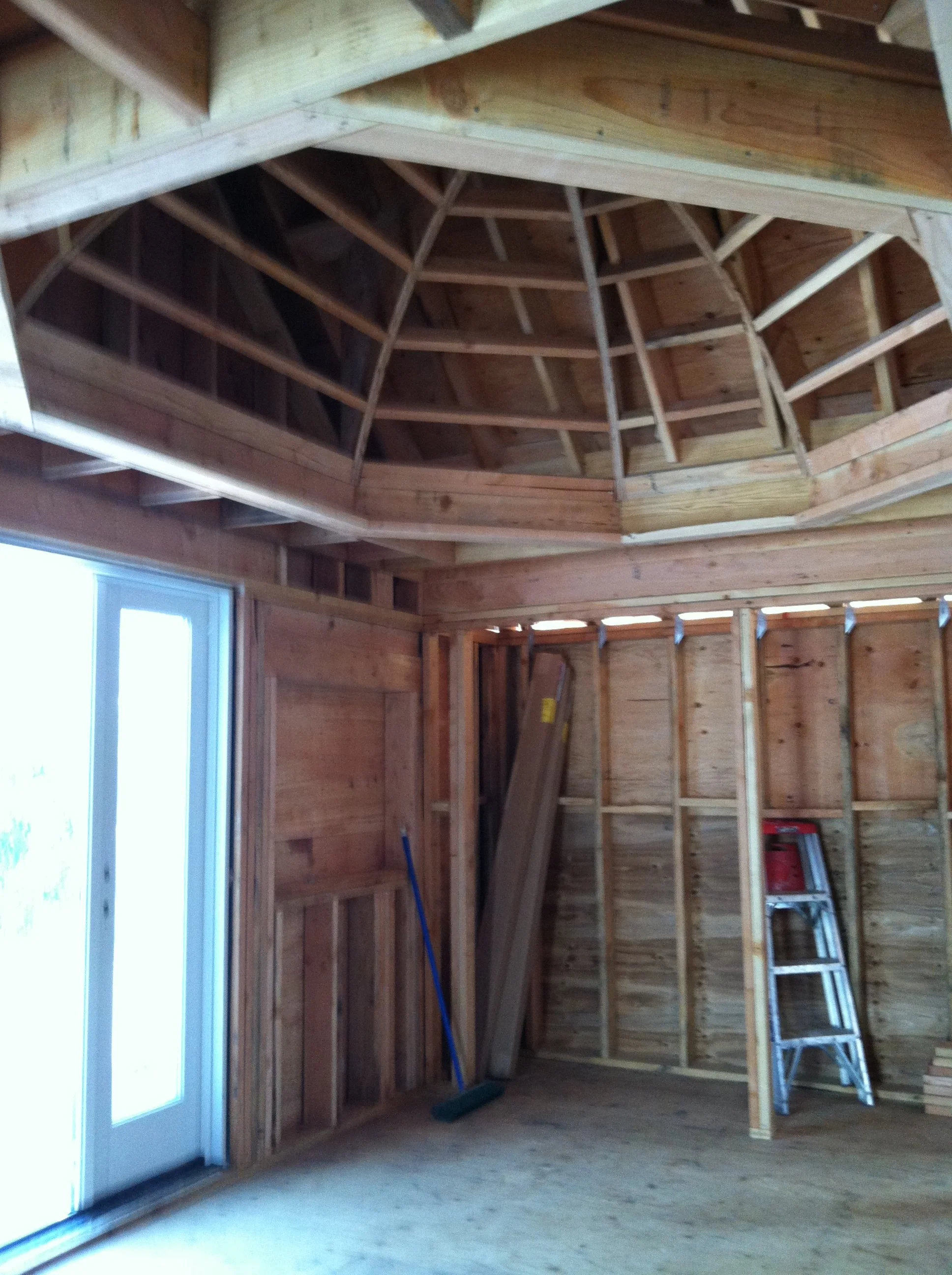Interior of a house under construction with exposed wooden framing, a ladder, and cleaning supplies.