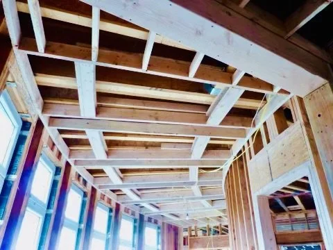 Interior view of a building under construction, showing exposed wooden framing and ceiling structure.