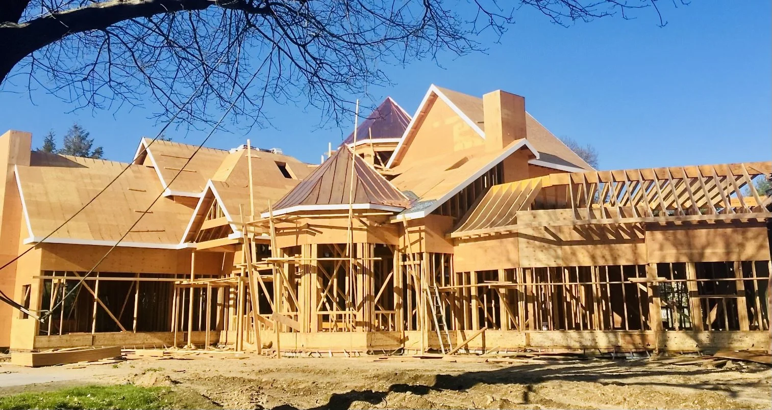 Wooden house under construction with scaffolding, blue sky, and leafless tree branches.