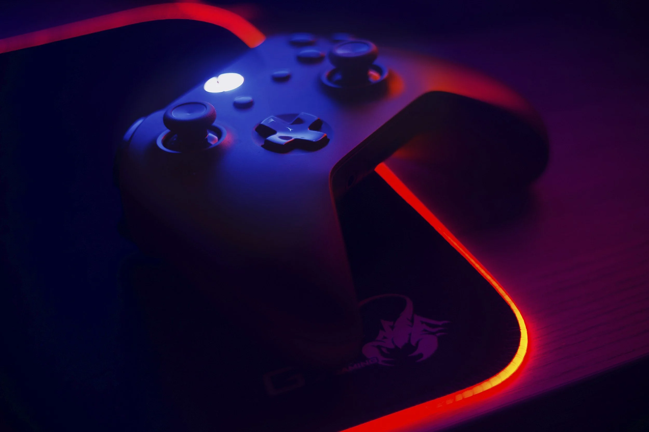 Close-up of a video game controller illuminated with red and blue LED lights, placed on a dark surface with a glowing red ring around it.