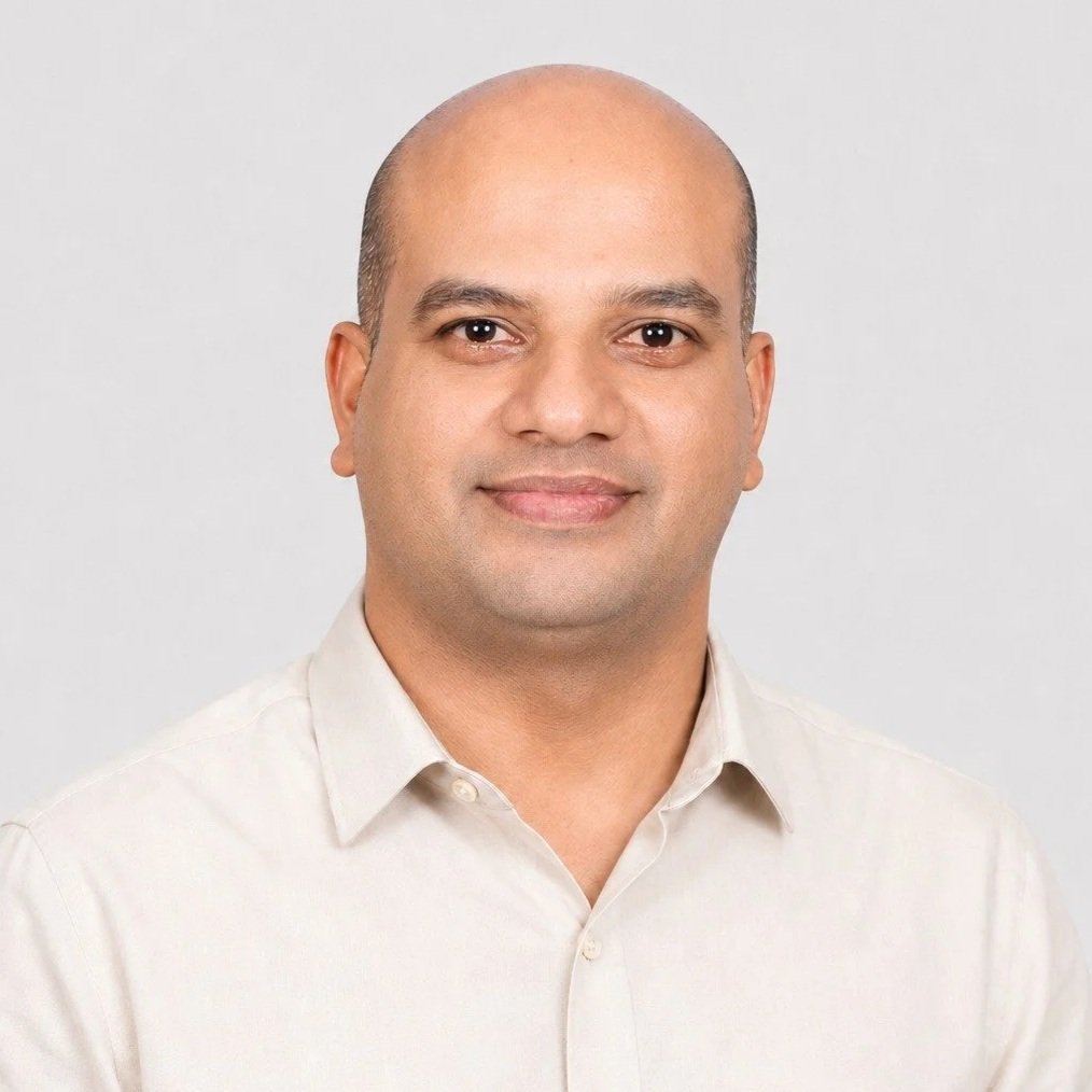 A portrait of a man with a neutral expression, wearing a light-colored collared shirt, against a plain gray background.