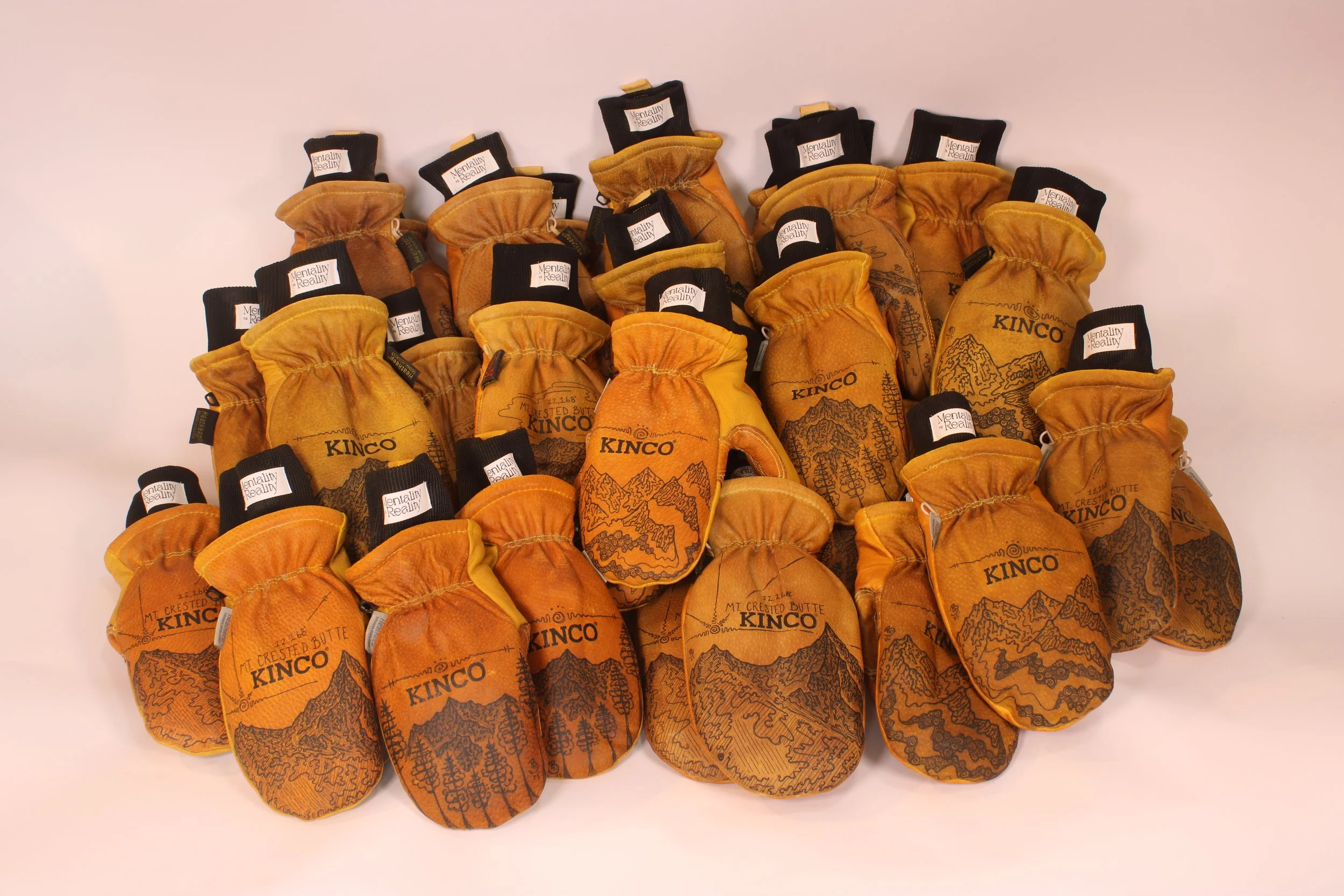 Multiple leather mittens with black cuffs and black tags with white text that reads 'Mentally Reality,' arranged on a white surface.