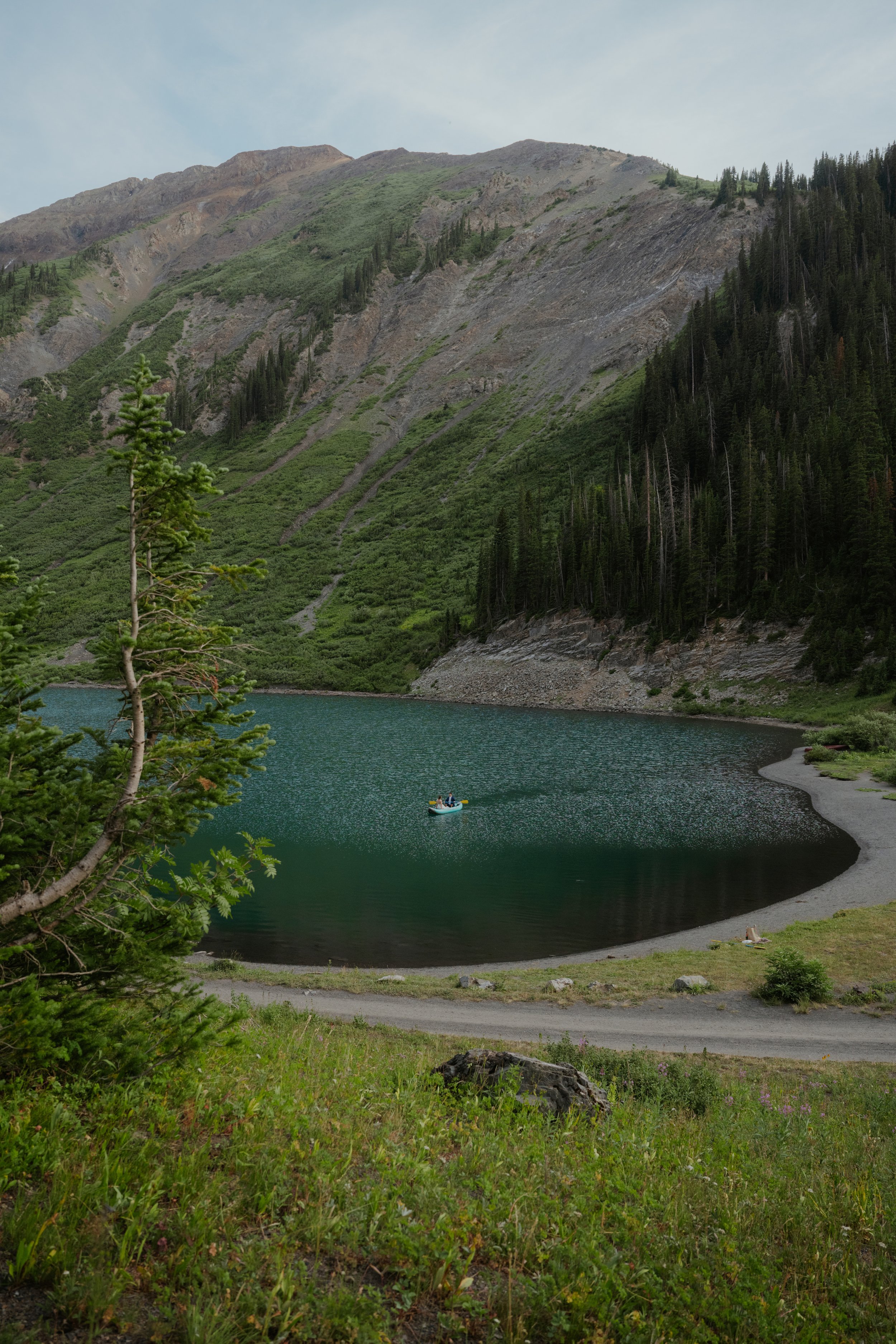 A scenic mountain landscape with a lake, a boat, green foliage, and a shoreline in the foreground.