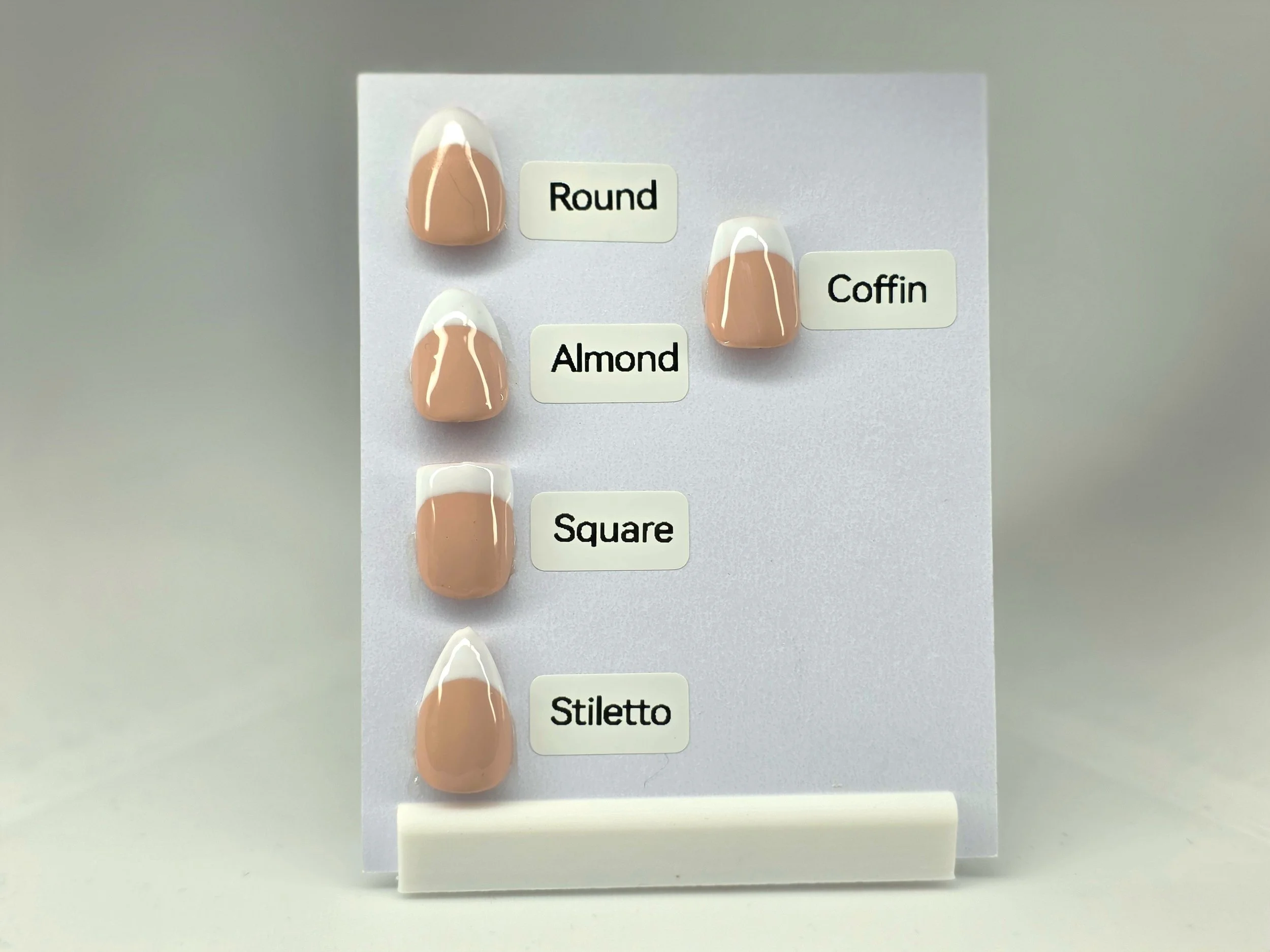 Three artificial nails painted with beige and white color, labeled as 'Round,' 'Coffin,' and 'Square,' displayed on white paper with corresponding labels.