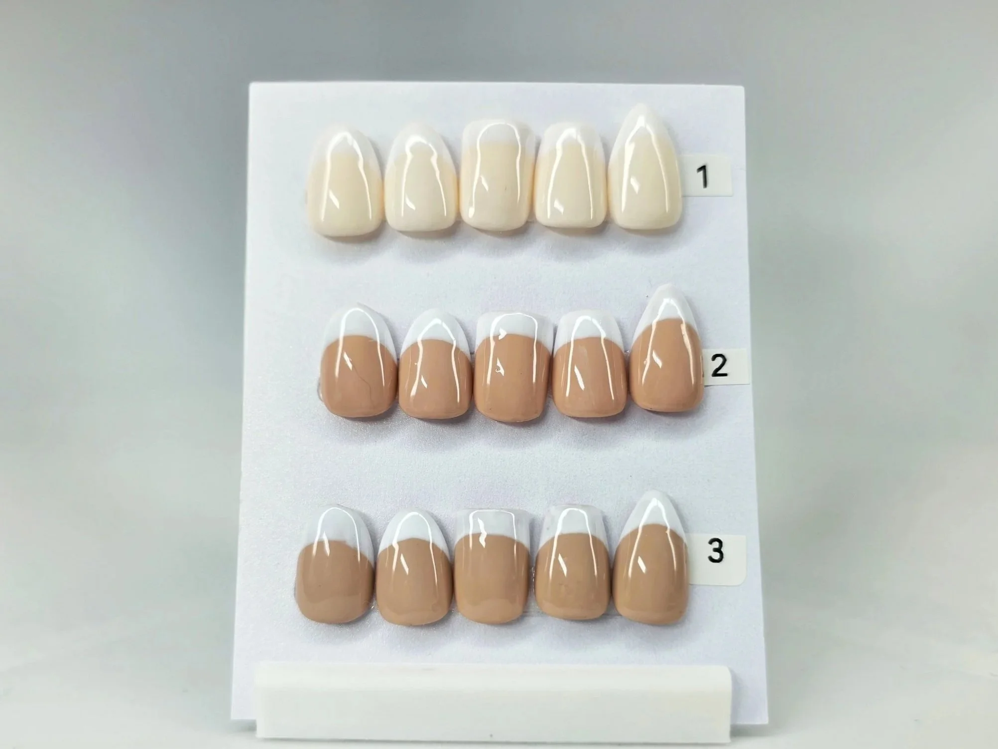 Display of three sets of artificial nails with different shades of nail polish on a white board, labeled 1, 2, and 3.