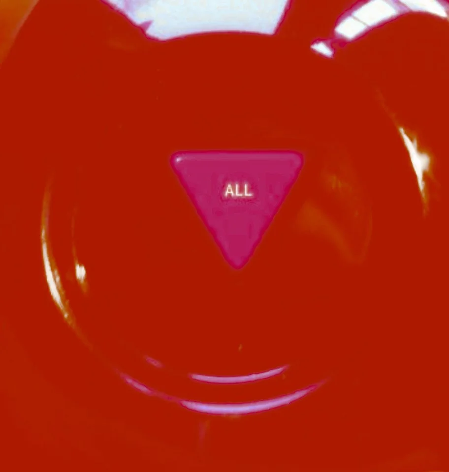 Close-up of a red button with a pink triangle shape in the center labeled 'ALL'.