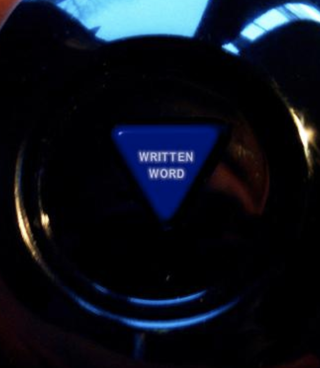 A blue triangular button with the words 'WRITTEN WORD' is situated on a black surface, possibly part of a control panel or electronic device.