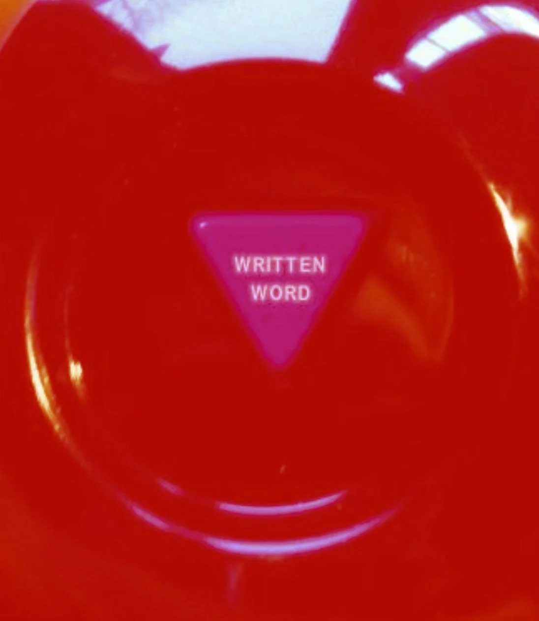 Close-up of a red button with a pink triangle in the center that says 'WRITTEN WORD'.