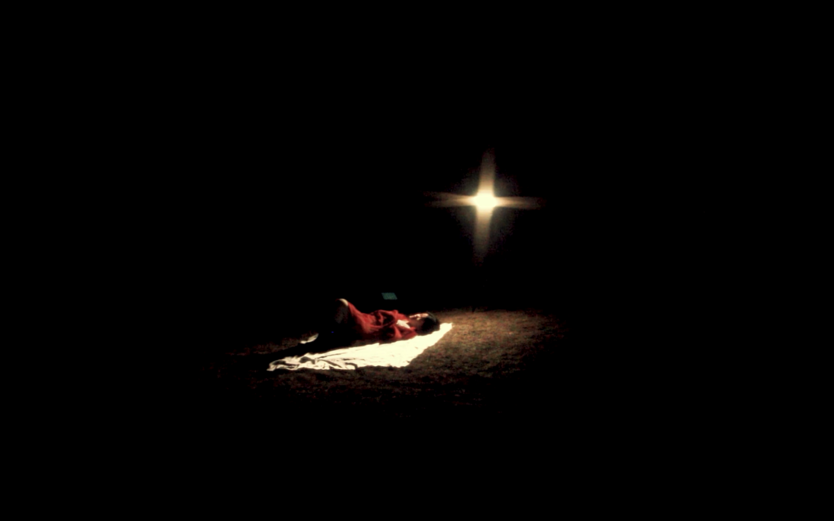 Person lying on a rug in a dark room with a single bright light source.