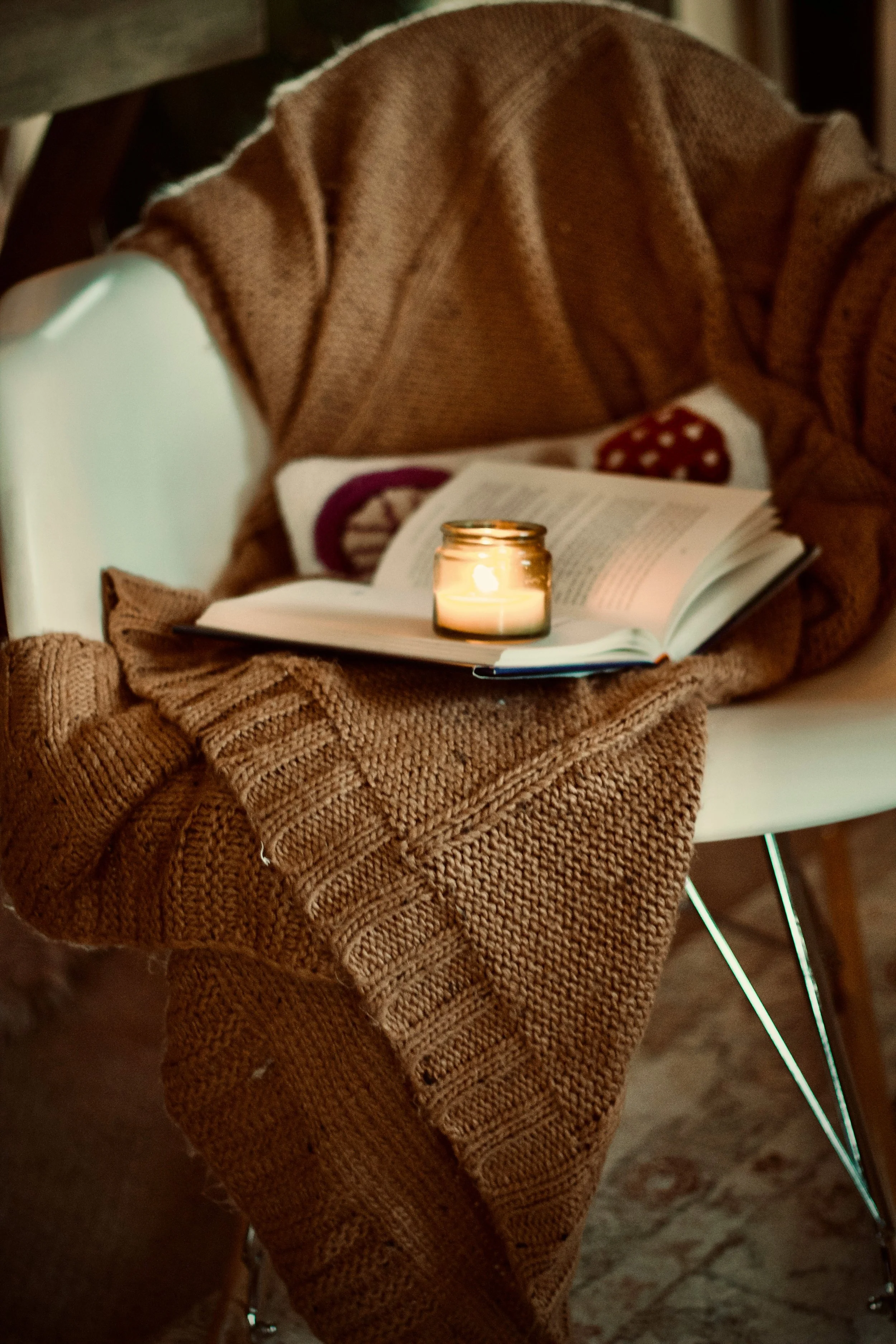 A candle and open book resting on a knit throw