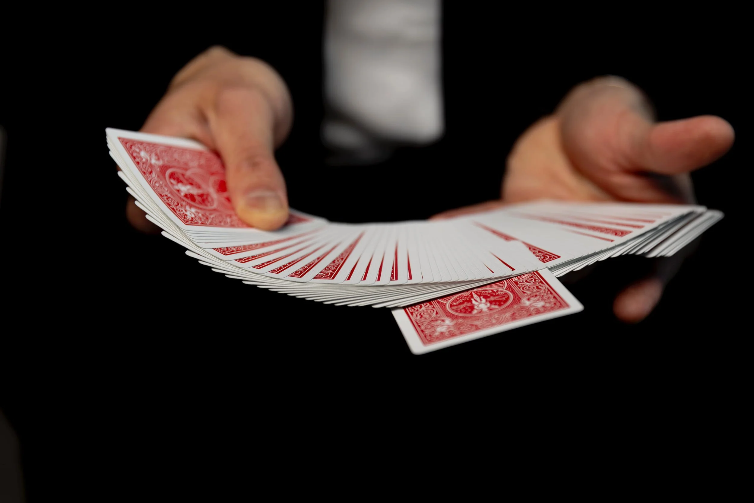 Close-up of a person holding a fan of red playing cards against a black background, with part of a white shirt visible.