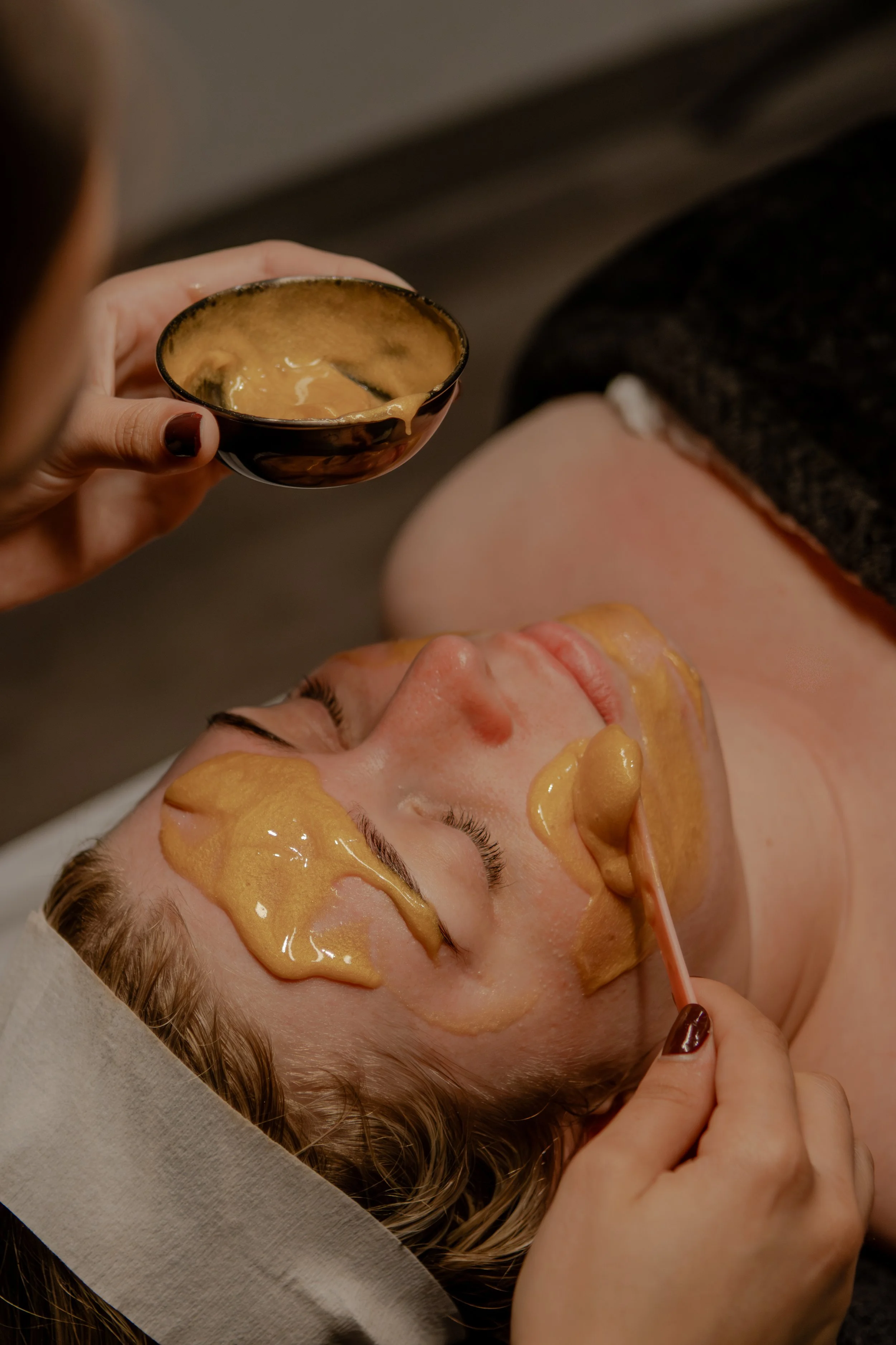 Woman giving a facial treatment with a golden facial mask as a spa or beauty treatment.