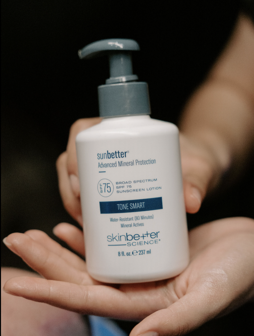 A hand holding a bottle of SunBetter advanced mineral protection sunscreen lotion with SPF 75, labeled as water-resistant for 80 minutes, from Skinbetter Science.