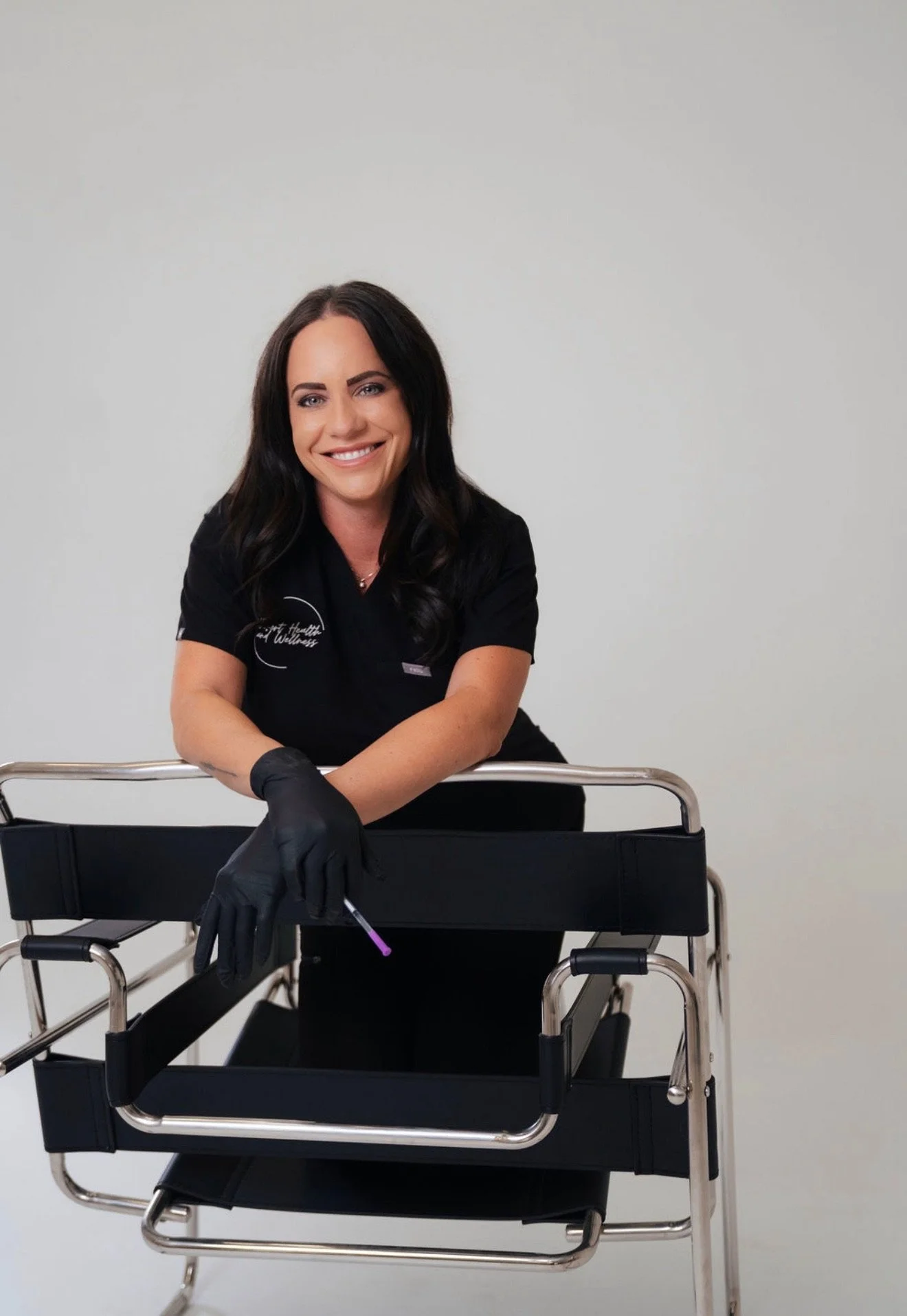 A woman with dark hair smiling, wearing black gloves and a black uniform, sitting in a wheelchair against a plain light gray background.