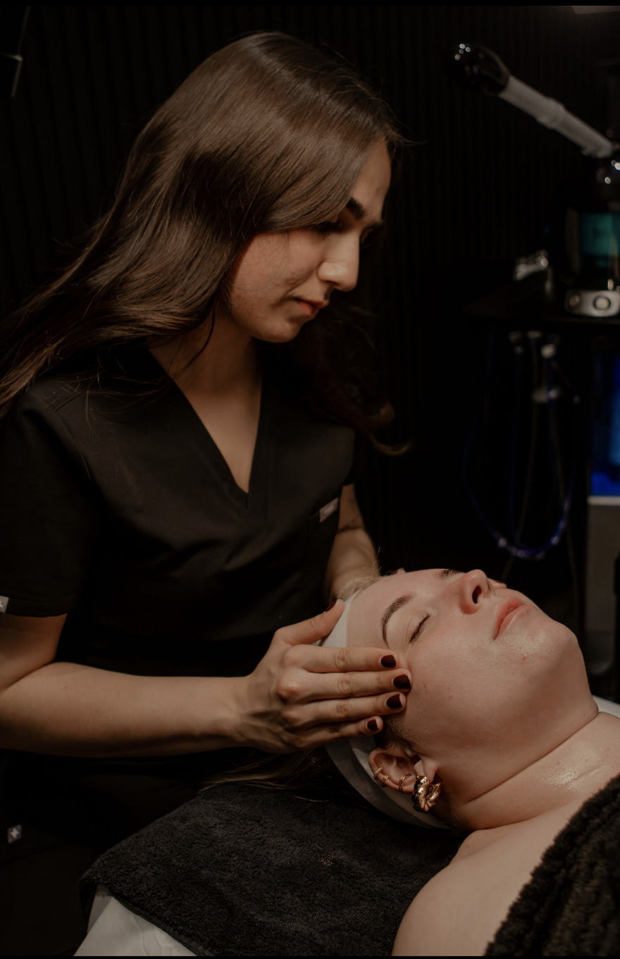 A woman receiving a facial treatment from a skincare professional in a spa or clinic setting.