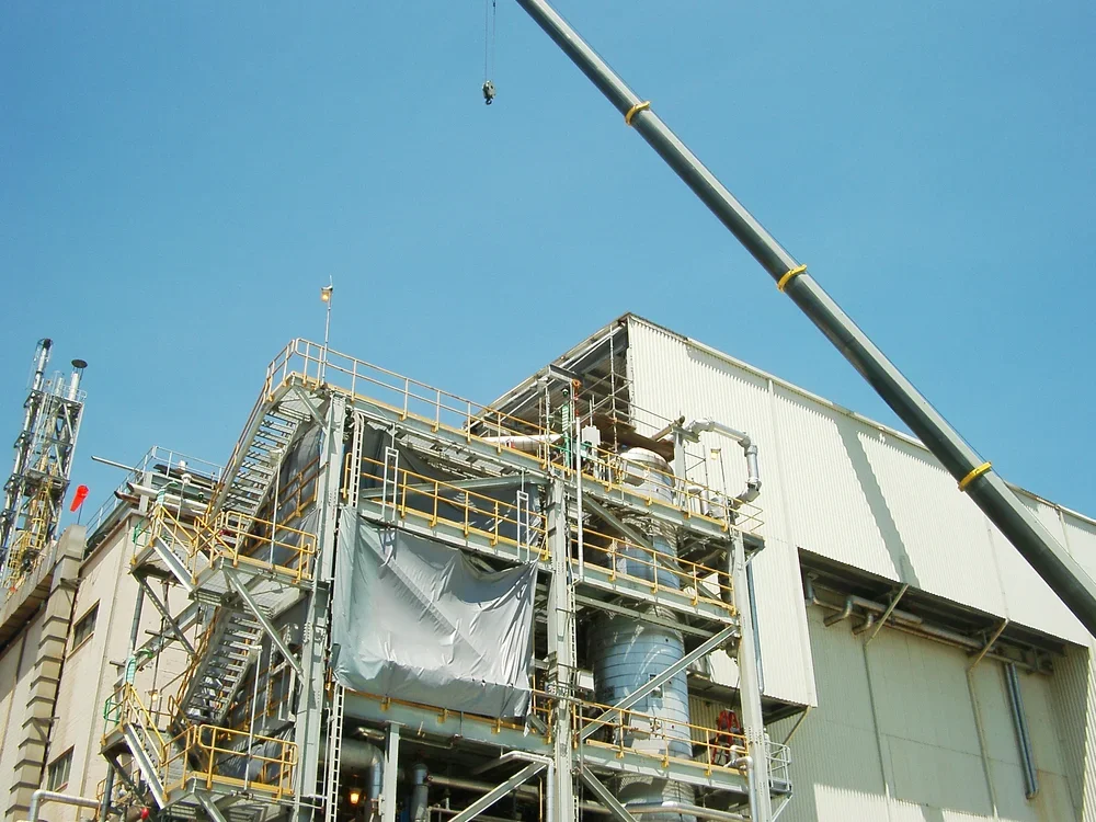 Industrial factory building with metal structures, pipes, and a crane arm extending across the sky.