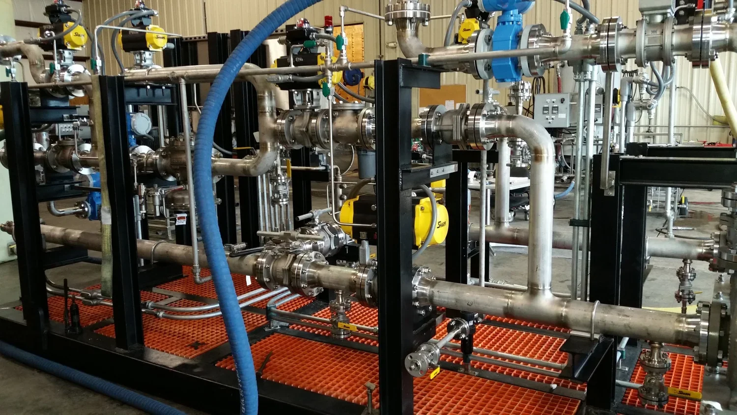 Industrial piping setup with metal pipes, valves, and gauges inside a factory or processing plant.