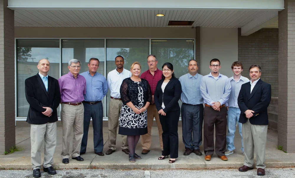Group of ten professionals standing outdoors in front of building with glass doors.