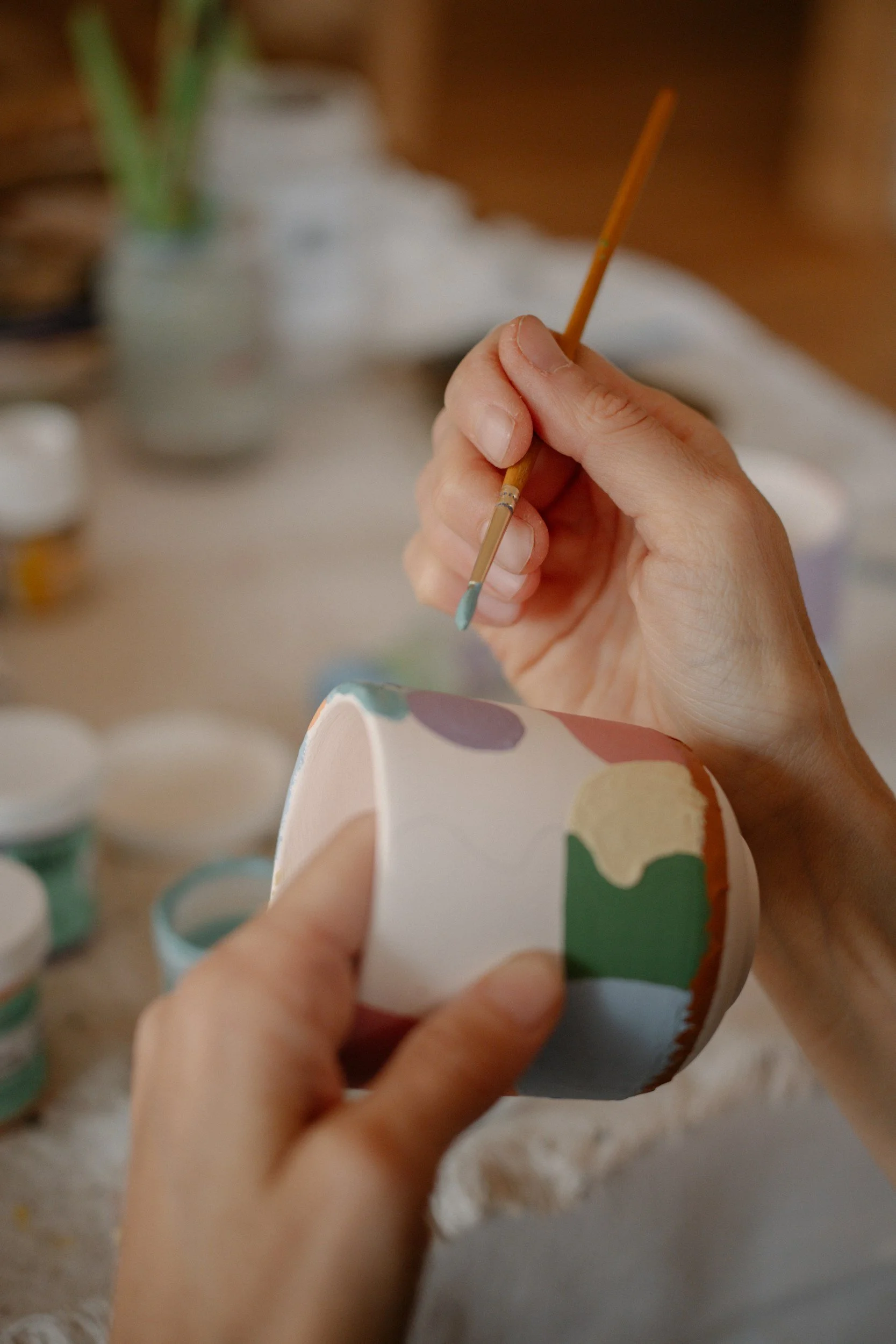 Person holding a paintbrush and painting a ceramic or paper craft object with a colorful, polka-dot pattern.