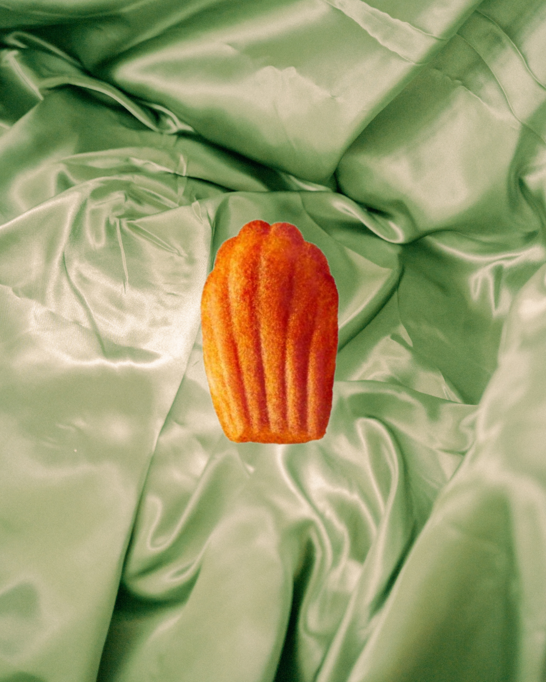 Un pastelito de vainilla con glaseado naranja, colocado sobre tela verde satinada con pliegues.