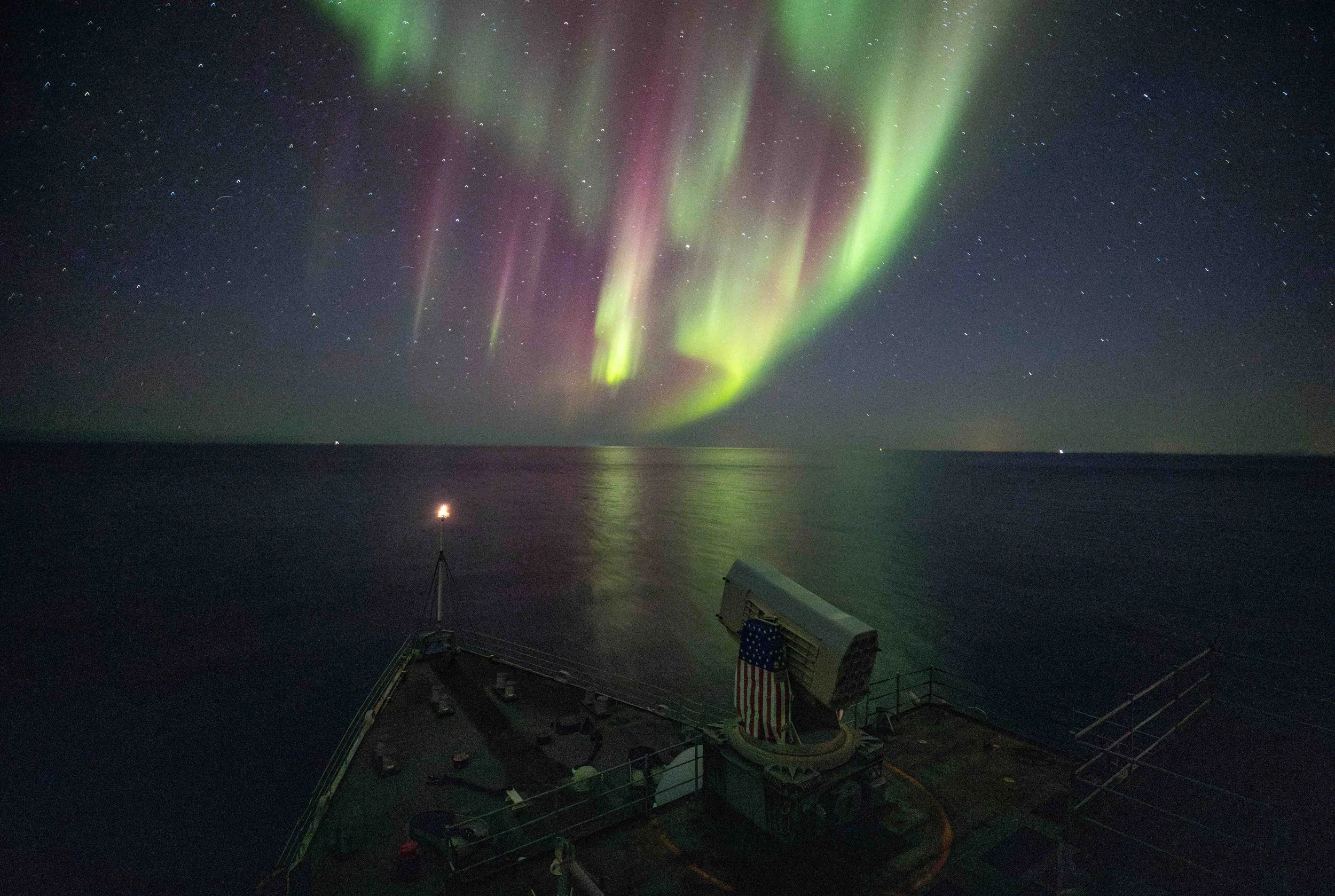 Northern lights (aurora borealis) illuminating the night sky over a body of water, with a ship's deck in the foreground.