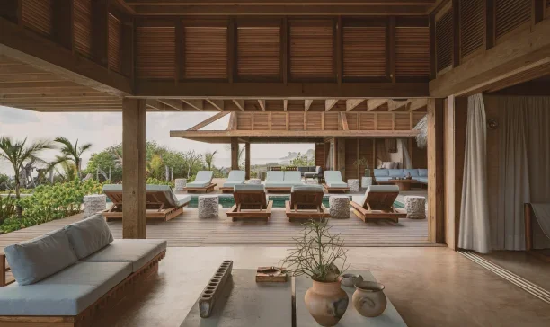 Open-air lounge with sun loungers and a poolside view, surrounded by trees and palm trees, in a tropical setting.