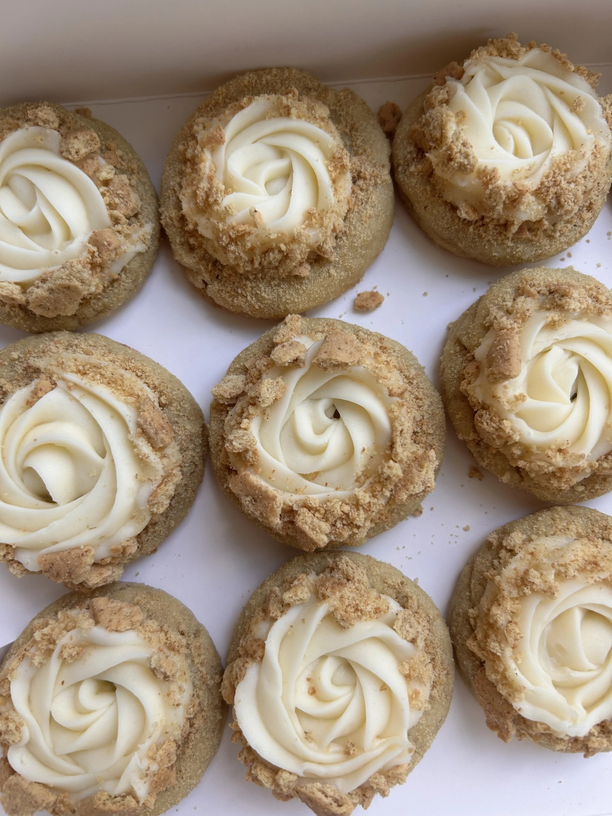Close-up of multiple cookies with vanilla frosting and crumbly topping on a white surface.