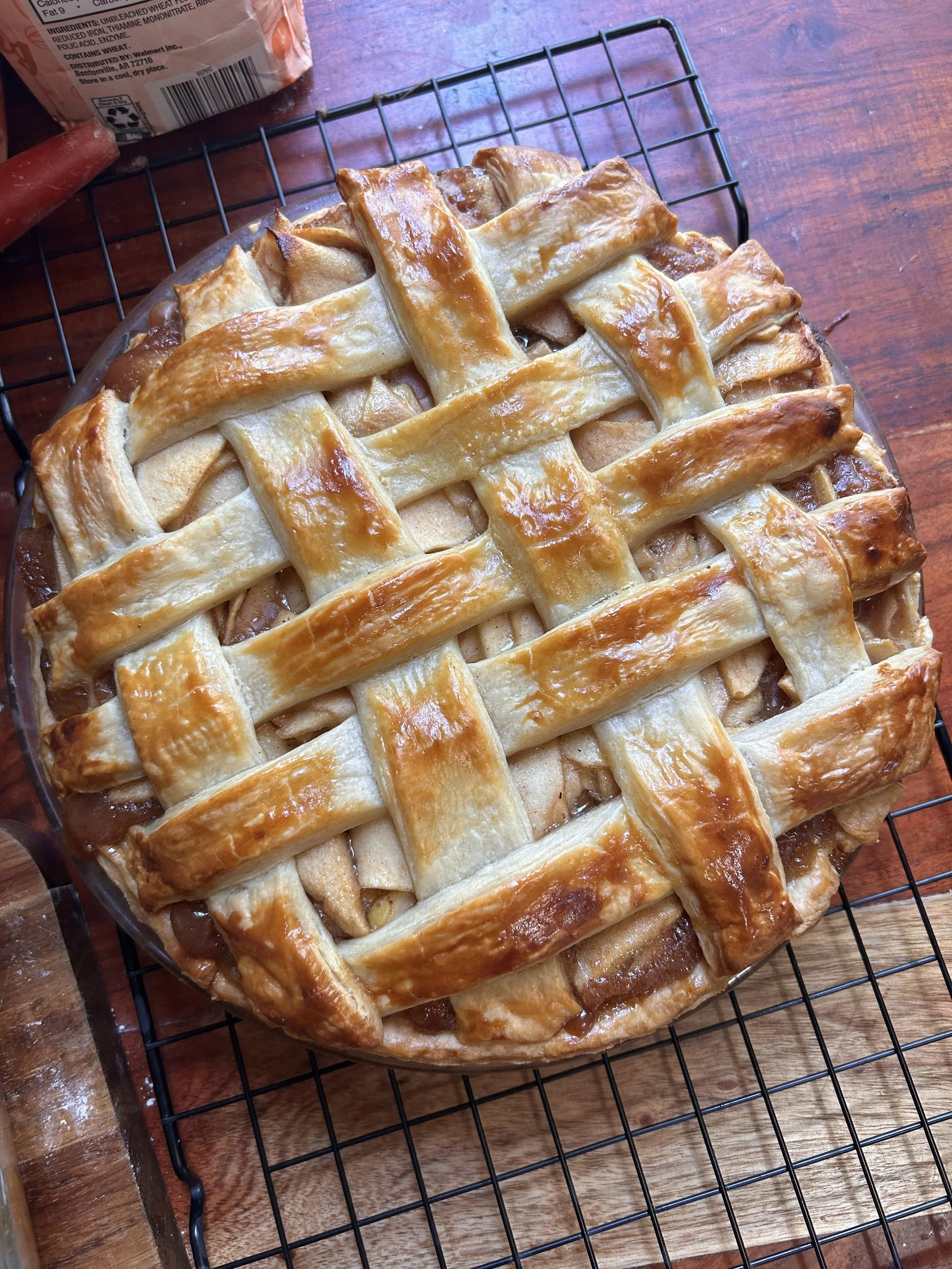 A lattice-topped apple pie cooling on a wire rack on a wooden table.