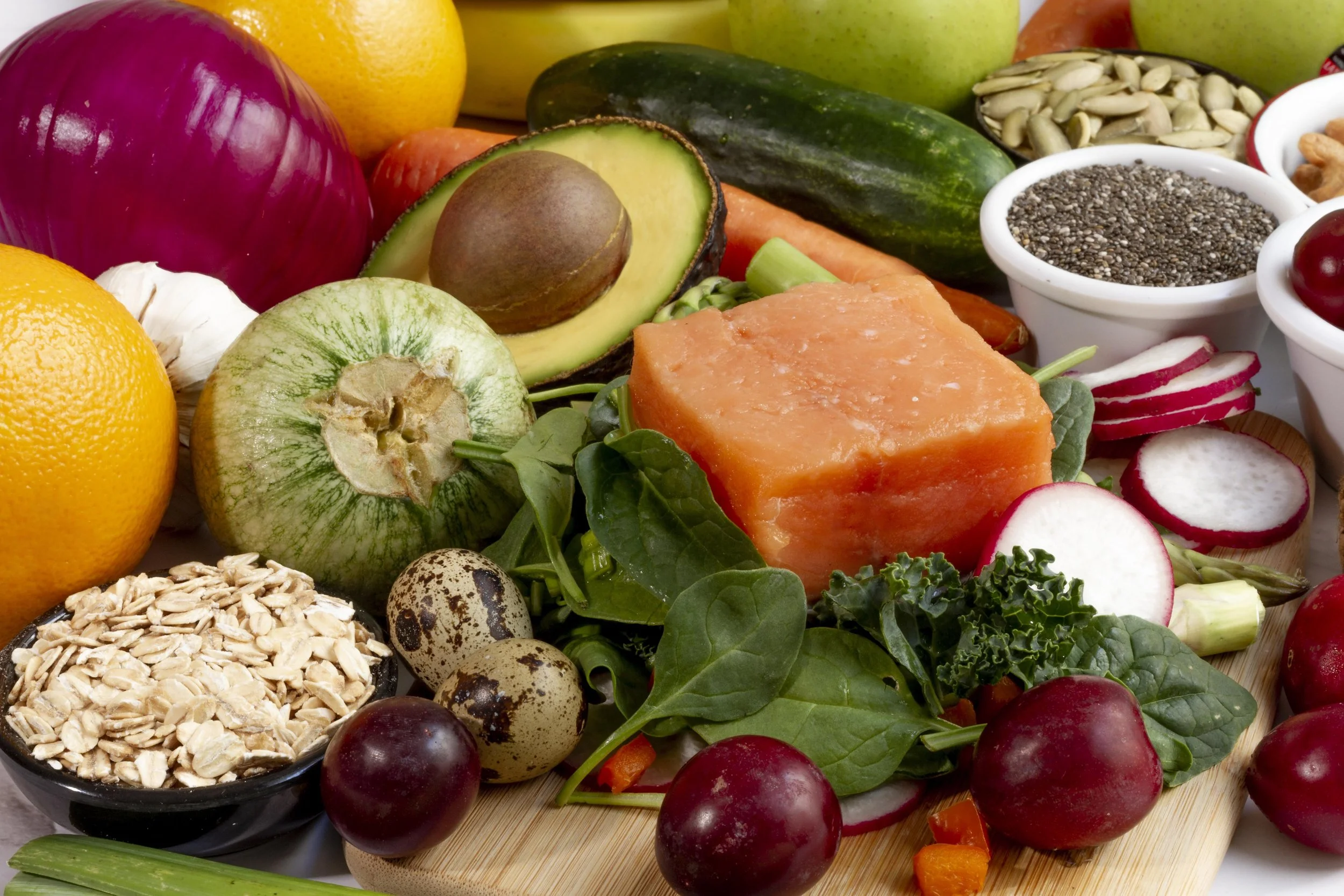 Assortiment de fruits, légumes, graines, et céréales tels que avocat, concombre, radis, papaye, graines de chia, graines de tournesol, potimarron, noix, et pommes.