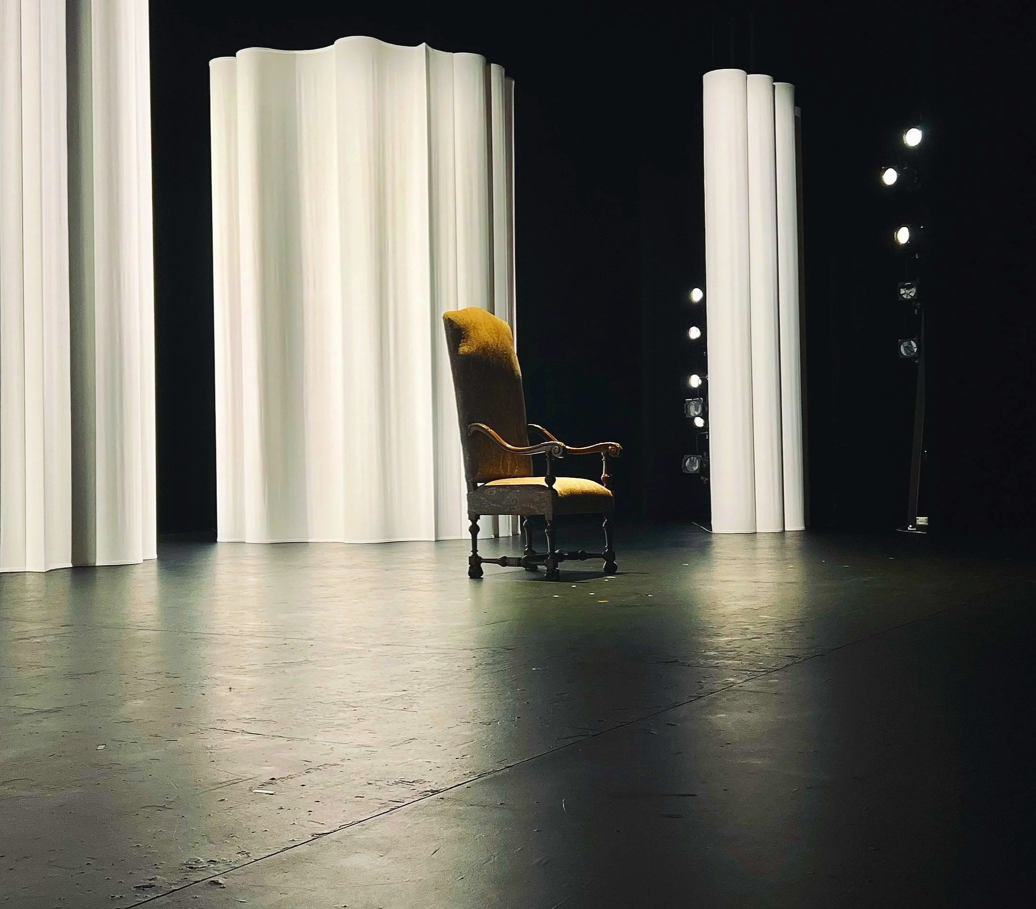 Empty theatre stage with a single vintage armchair, used to represent theatre reviews and performance criticism.