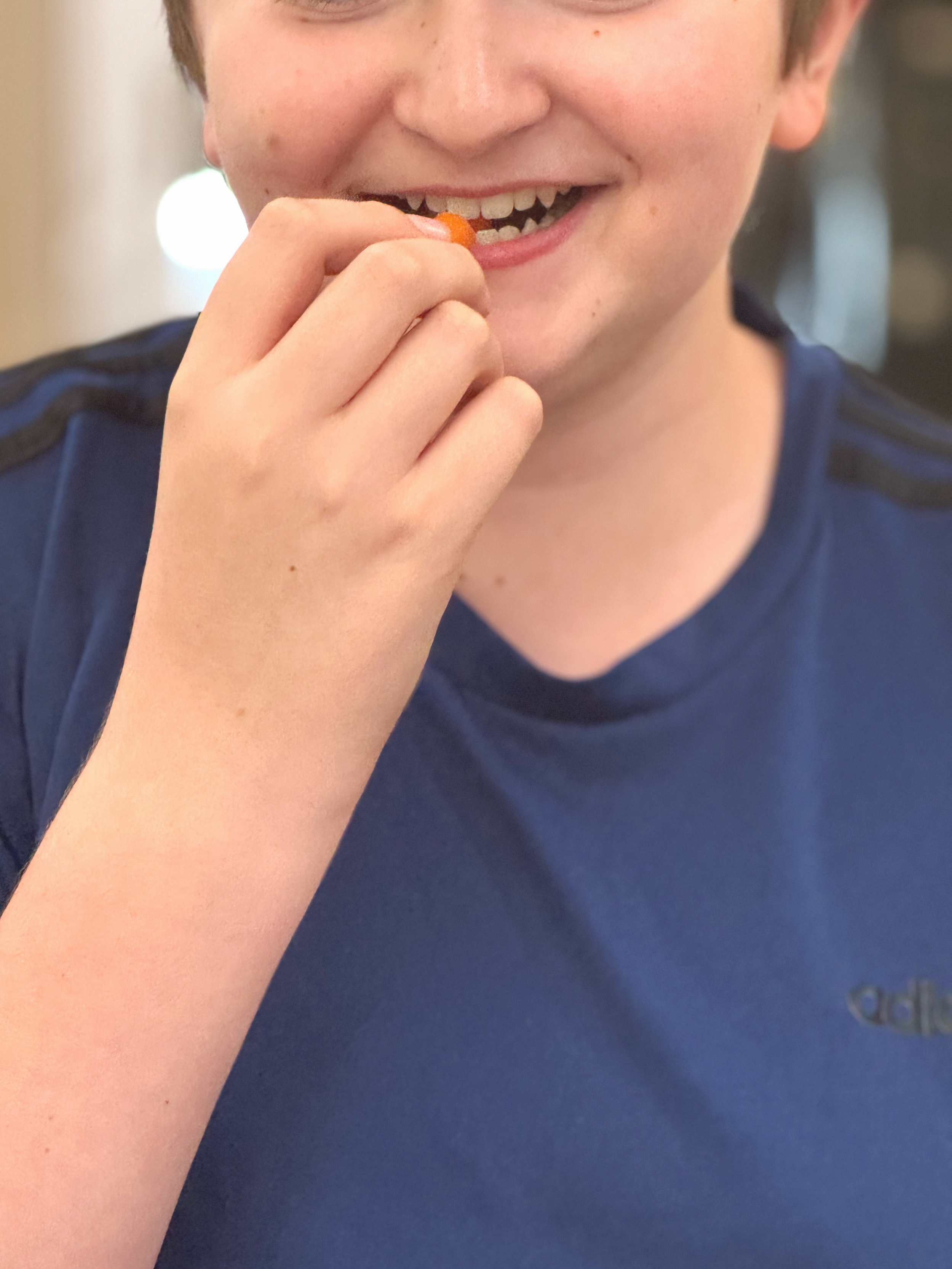 Close-up of a person smiling and biting into a snack, with a blurred background.