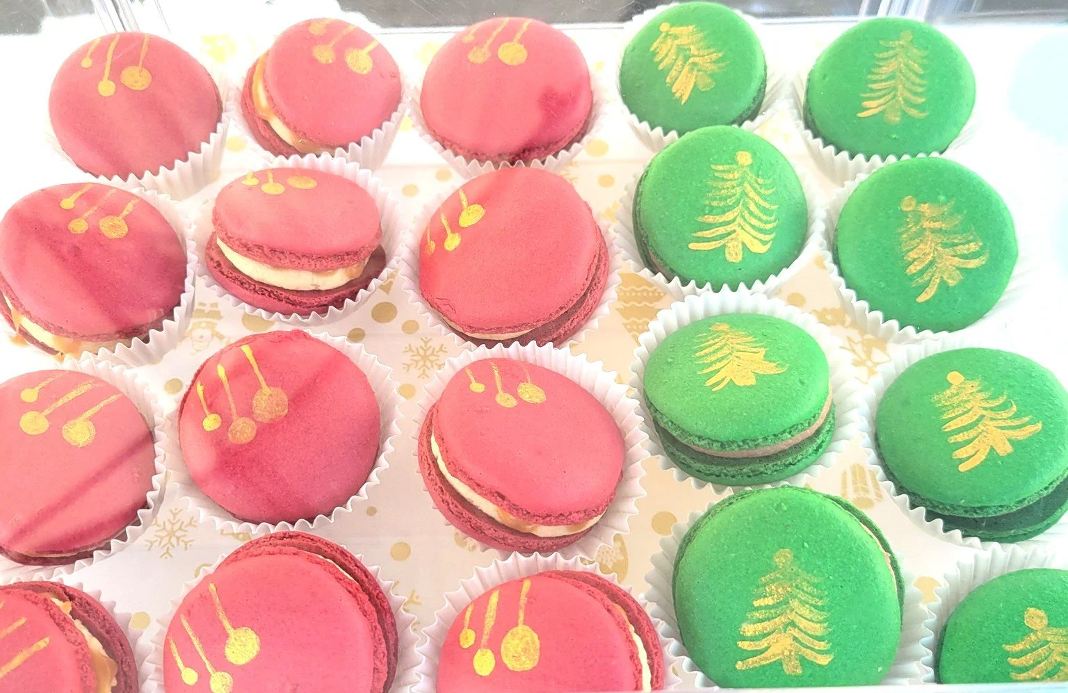 Rows of pink and green Christmas-themed macarons with gold holiday decorations on top.