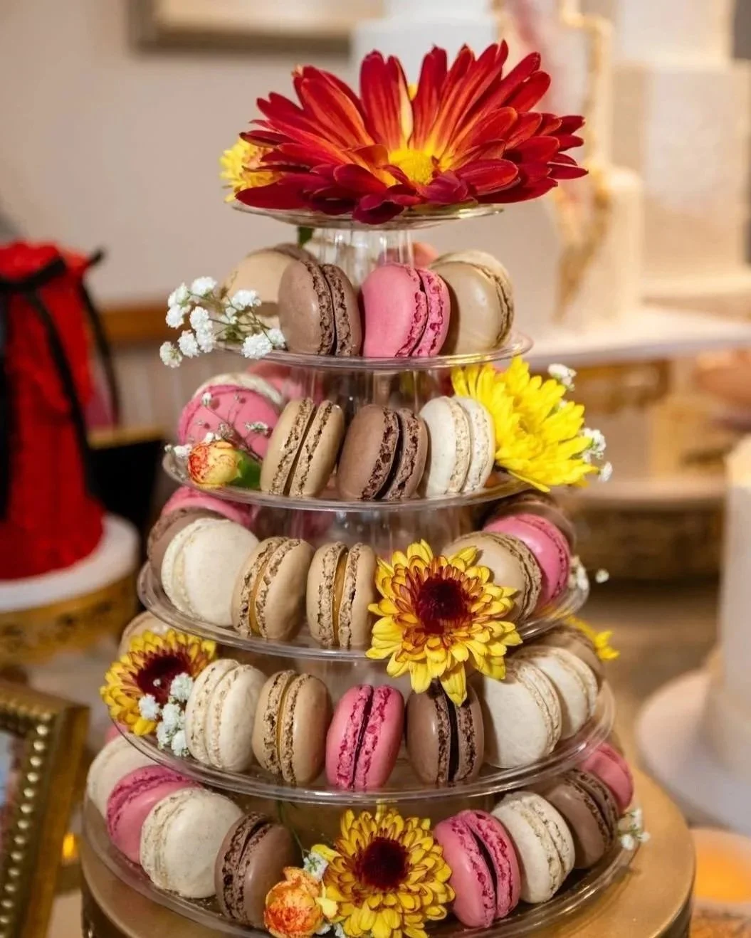 A tiered stand filled with colorful macarons and decorated with vibrant flowers.