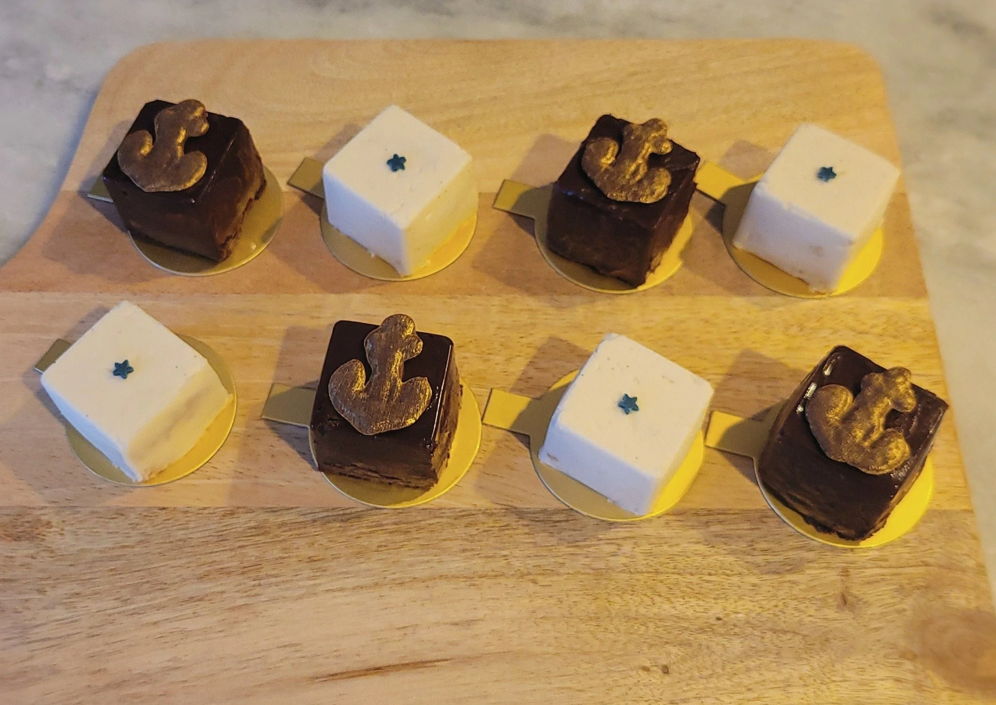 Assorted small square desserts with different icing and toppings on a wooden surface