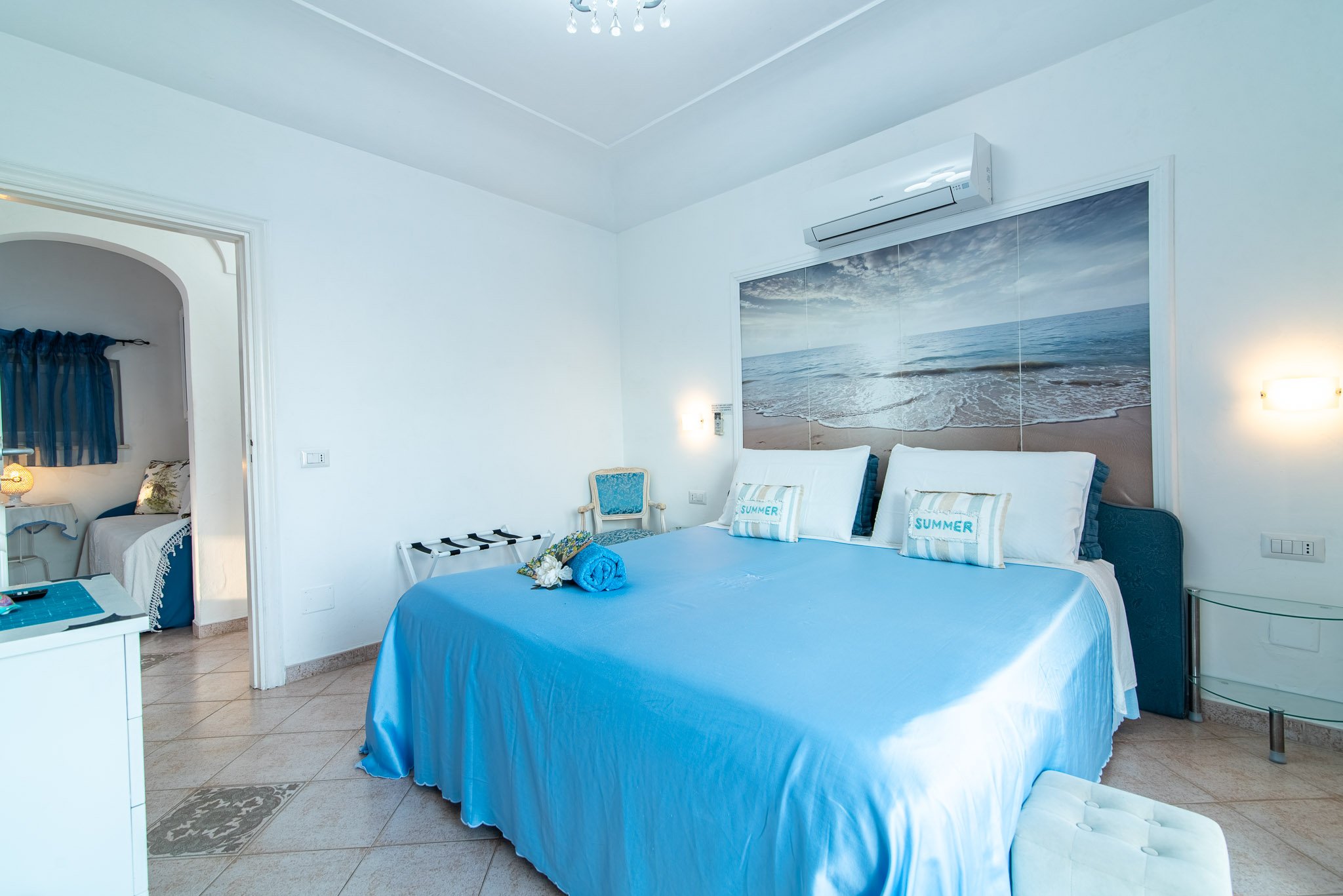 Bright marine style guest bedroom at a Capri boutique villa featuring a blue double bed, beach wall mural, and a connecting room door.