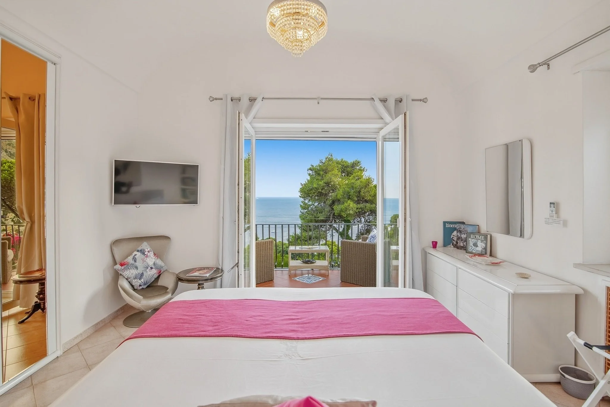 Bright bedroom interior at a Capri holiday home showing a double bed, white dresser, and open balcony ocean view.