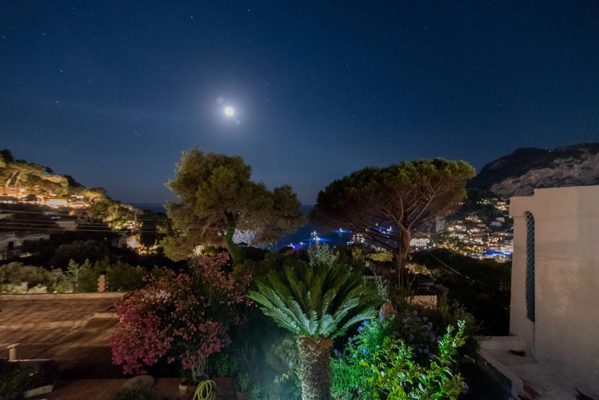Romantic night view of the illuminated Capri coast and garden under full moonlight from a luxury retreat terrace.