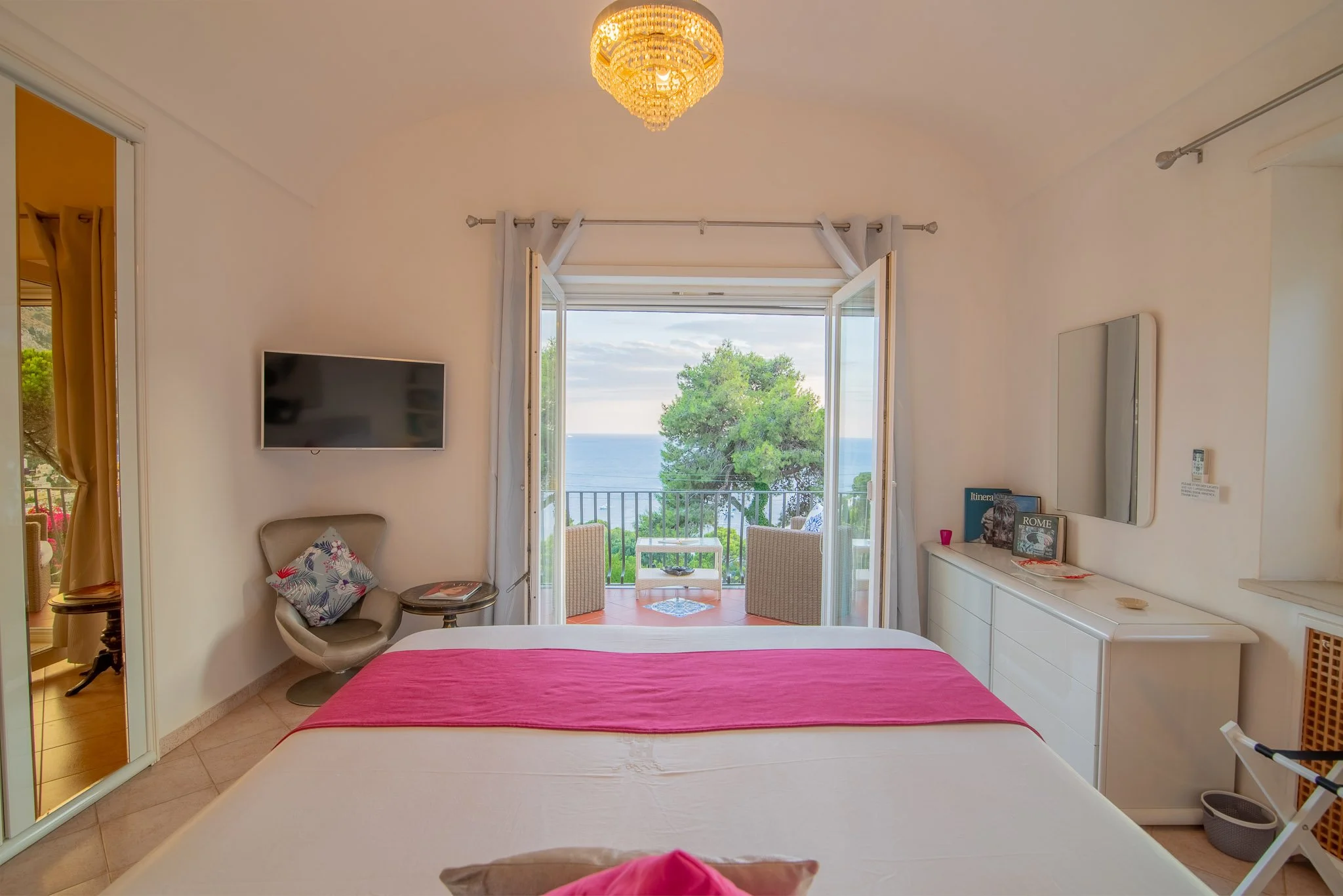 Bright bedroom interior at a Capri holiday home showing a double bed, white dresser, and open balcony ocean view.