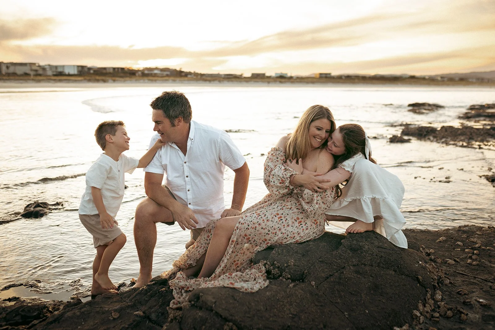 A family enjoying a sunset on the beach, hugging and playing on rocks and water.