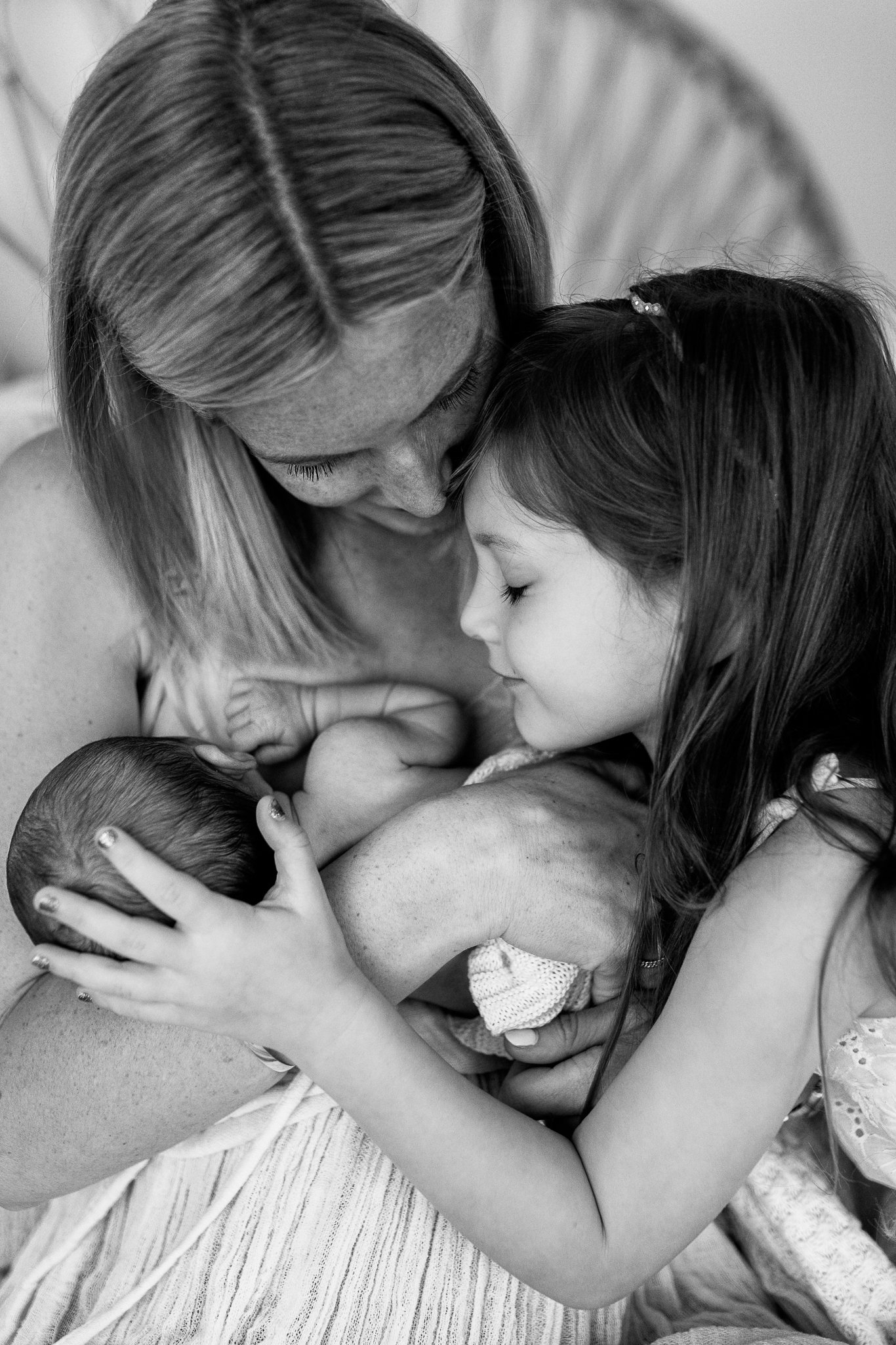 A woman is holding a newborn baby close to her chest, with her eyes closed and forehead touching the baby's head, showing a tender moment of bonding.