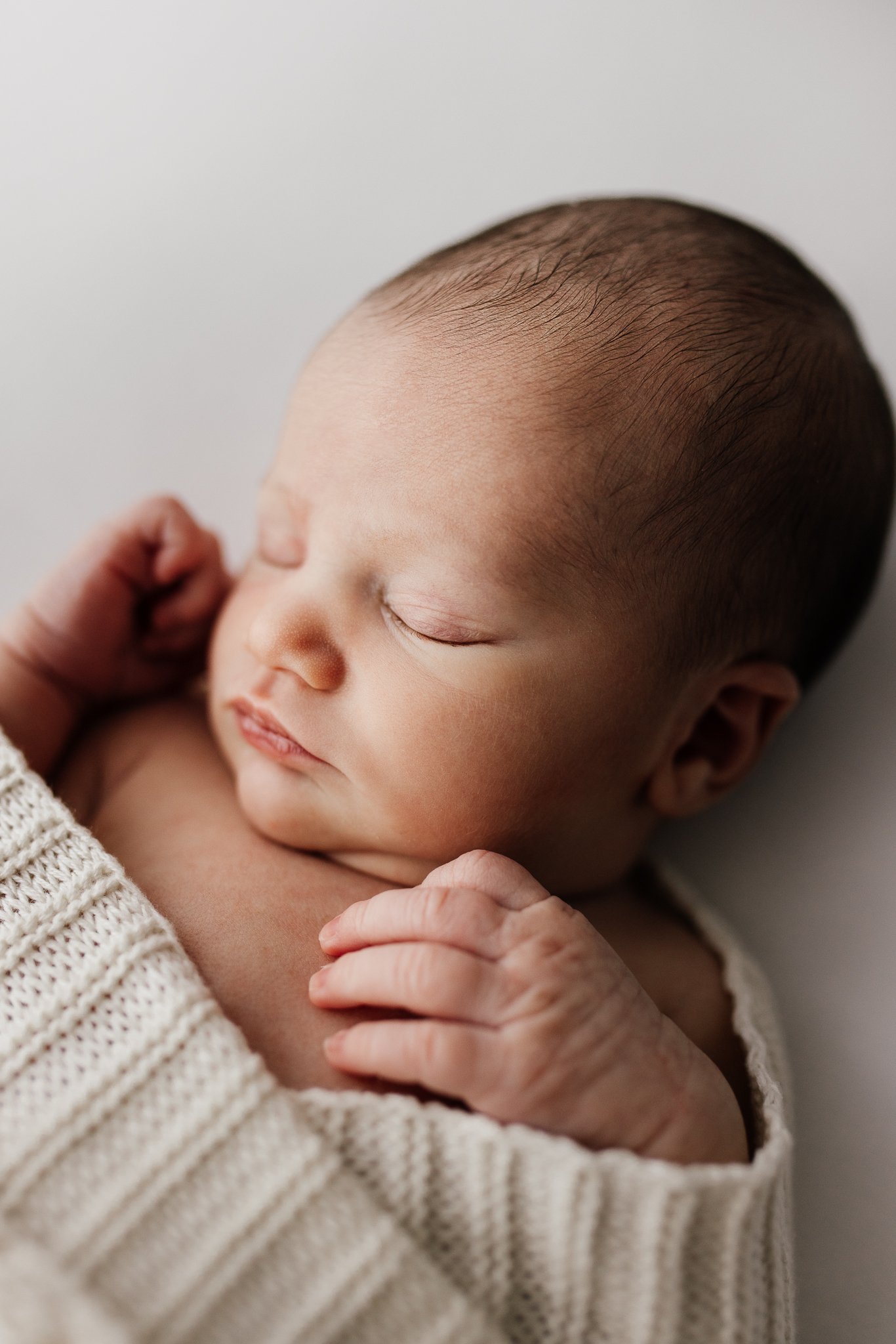 Close-up of a sleeping baby's face with closed eyes, smooth skin, and sparse hair, wearing a knit sweater.