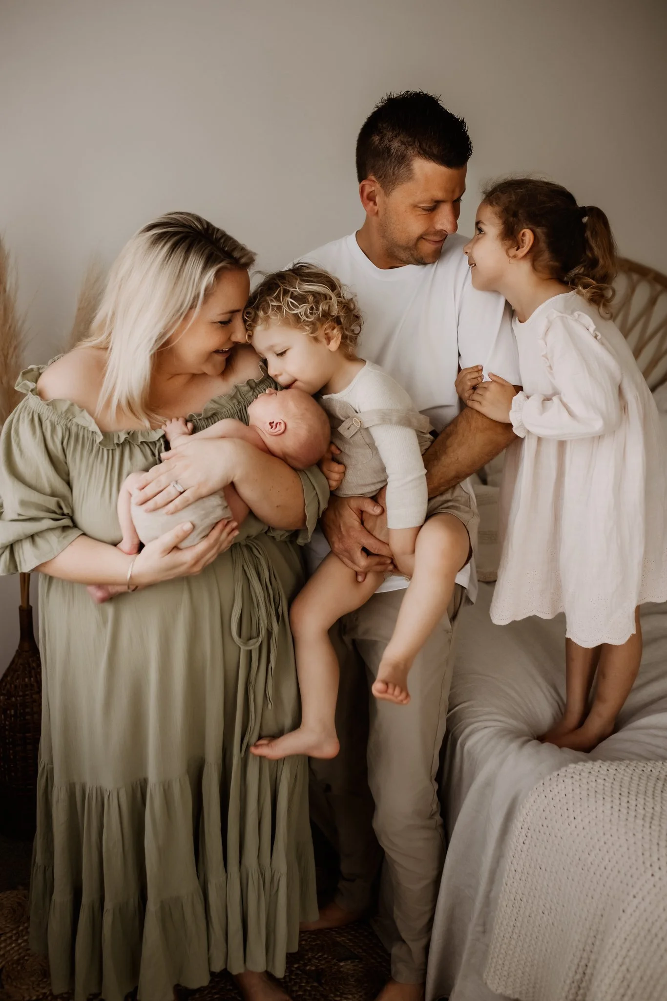 A multi-generational family gathered together in a cozy, neutral-toned room, sharing a tender moment as they embrace each other warmly, with a mother holding a newborn, a father smiling at a young girl, and other children all looking affectionately a