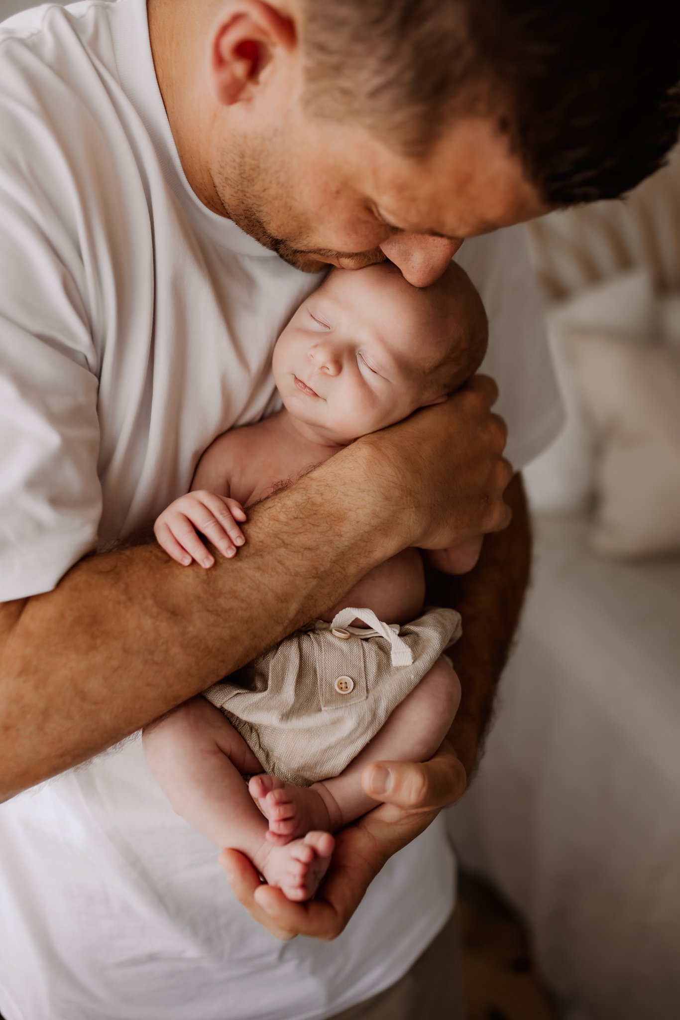 A man holding a sleeping baby close to his face, both with closed eyes, in a tender moment.