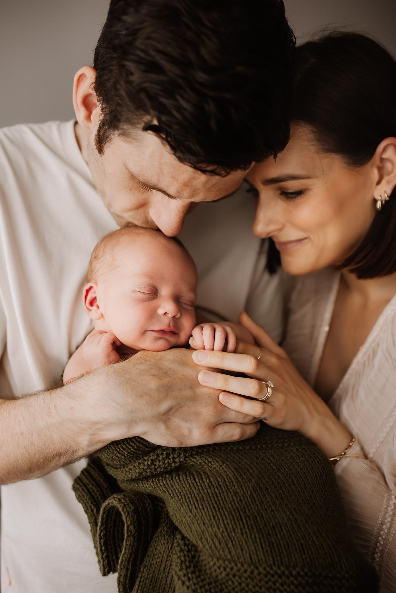 A couple lovingly holding their sleeping newborn baby close to their chests, with their foreheads touching, in a tender moment of family bonding.